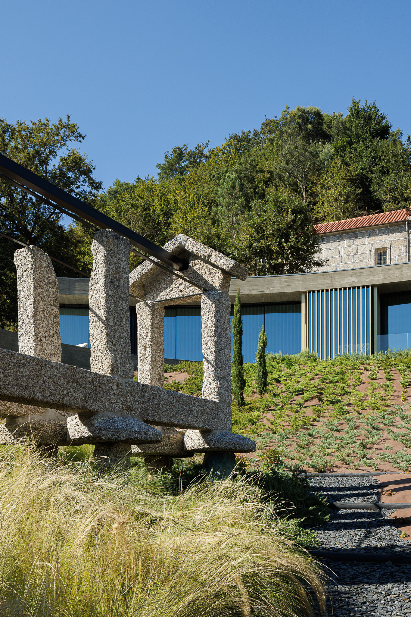 Granite water feature with carved channels beside gravel path and planted slope with grasses