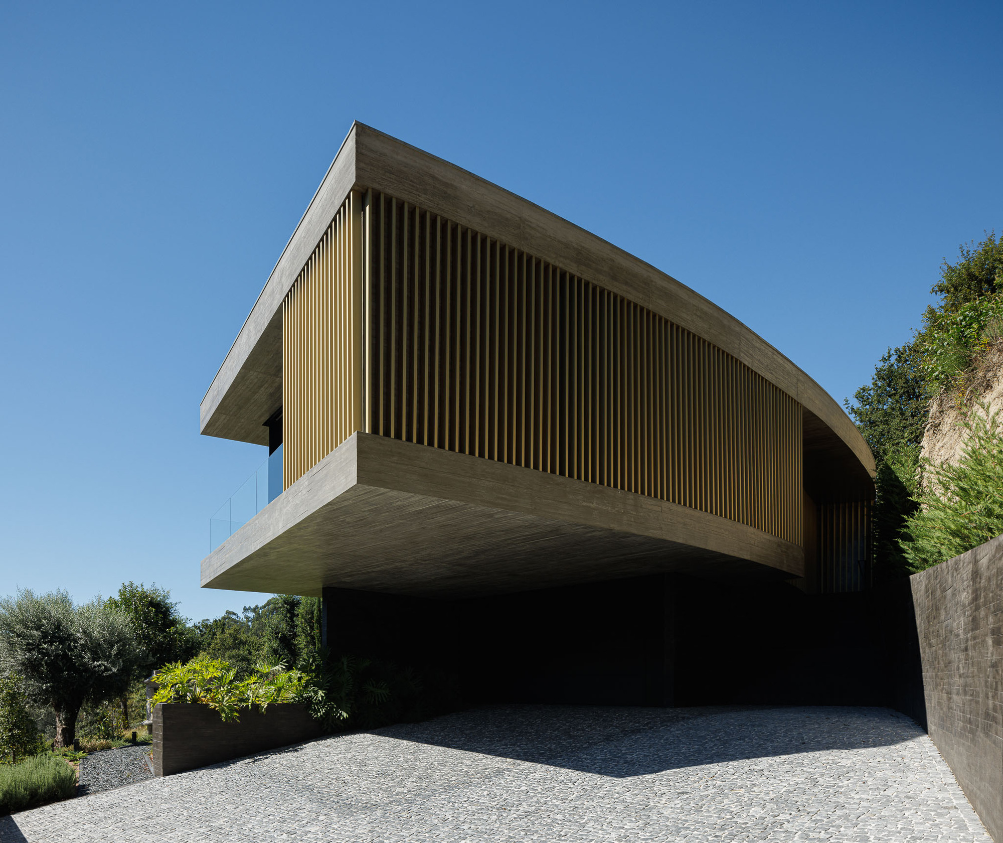 Cantilevered concrete upper volume with vertical timber slat cladding over gravel terrace