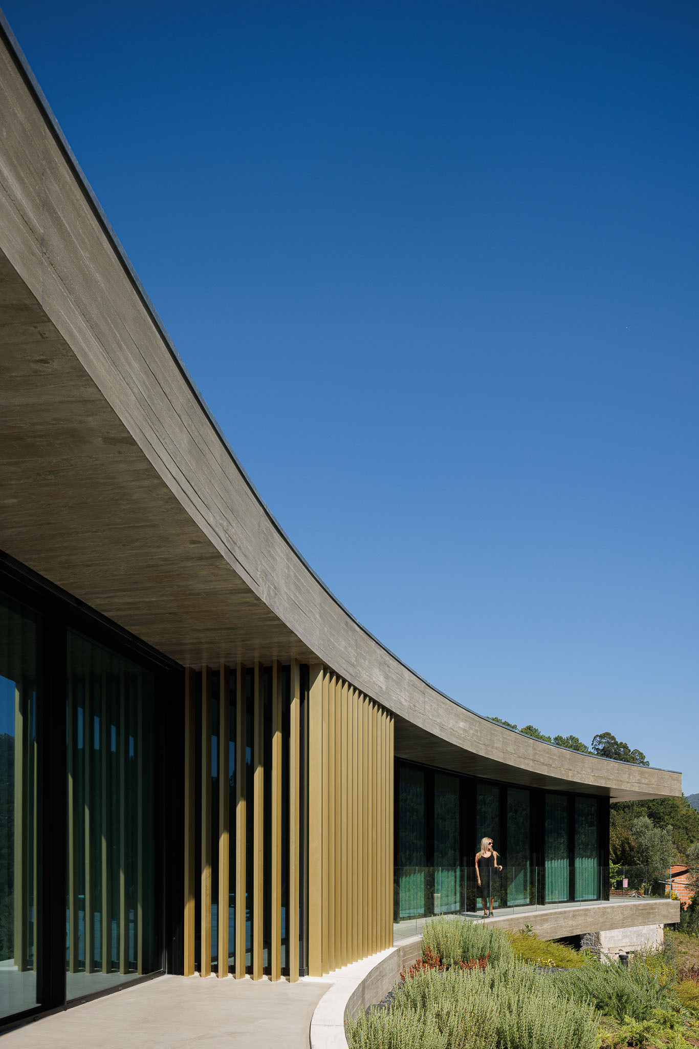 Curved terrace with timber brise-soleil and glazed facade with a figure standing beyond