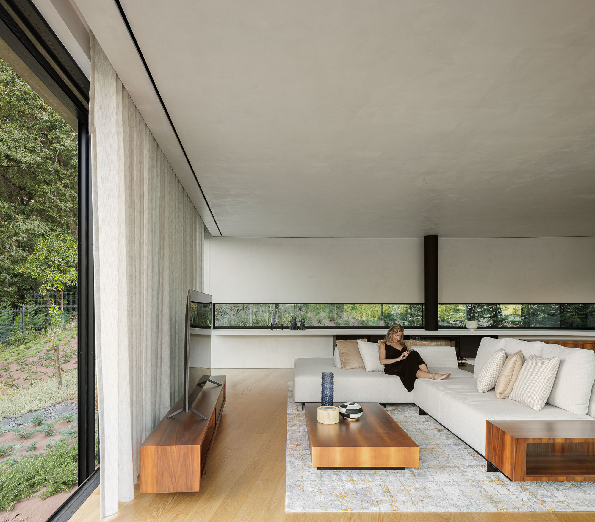 Living room with floor-to-ceiling glazing, sheer curtains, and a person seated on a low white sofa