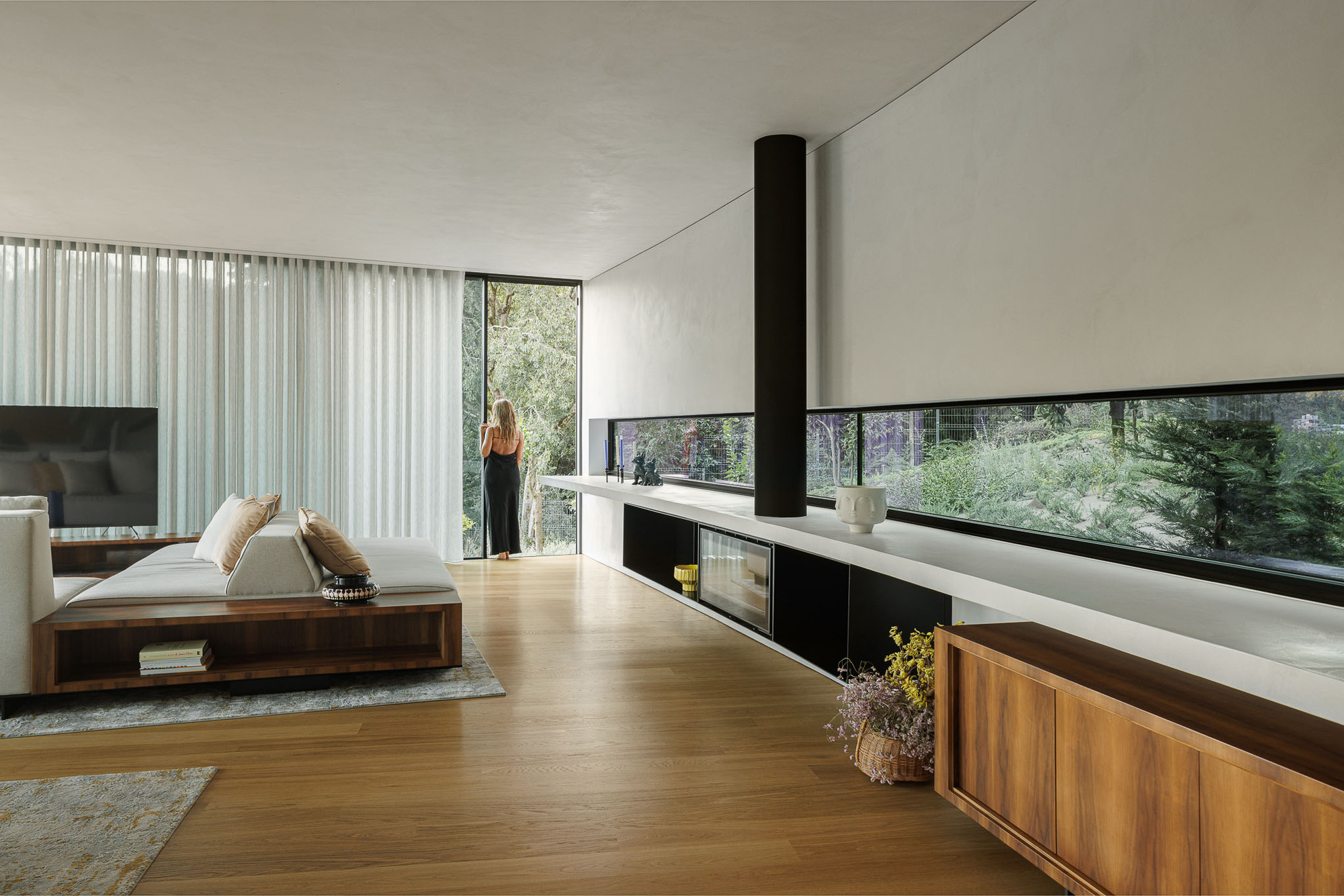 Living space with a black cylindrical flue and horizontal ribbon window framing garden views