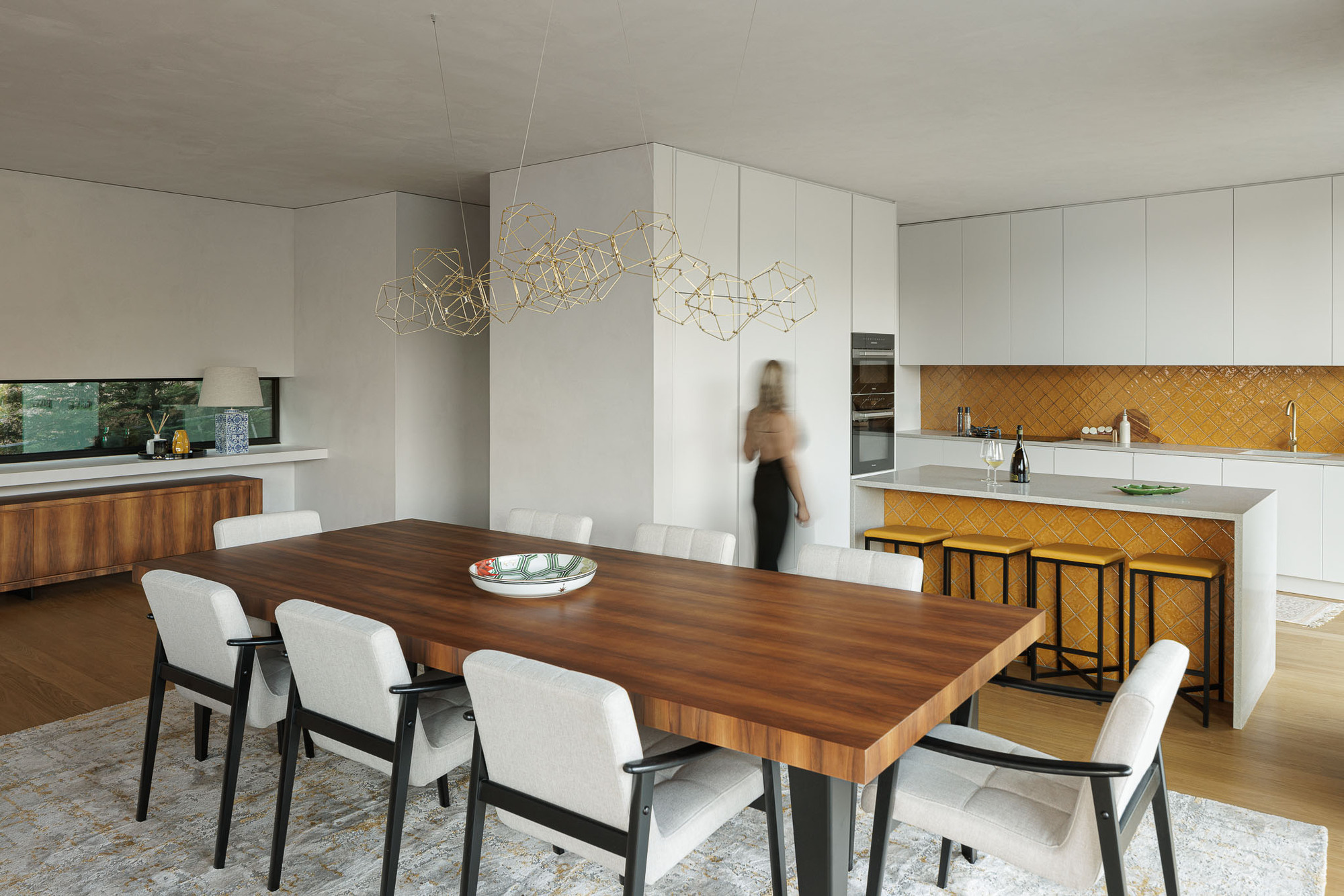 Dining area with a walnut table and white cabinetry with yellow tile backsplash in the kitchen
