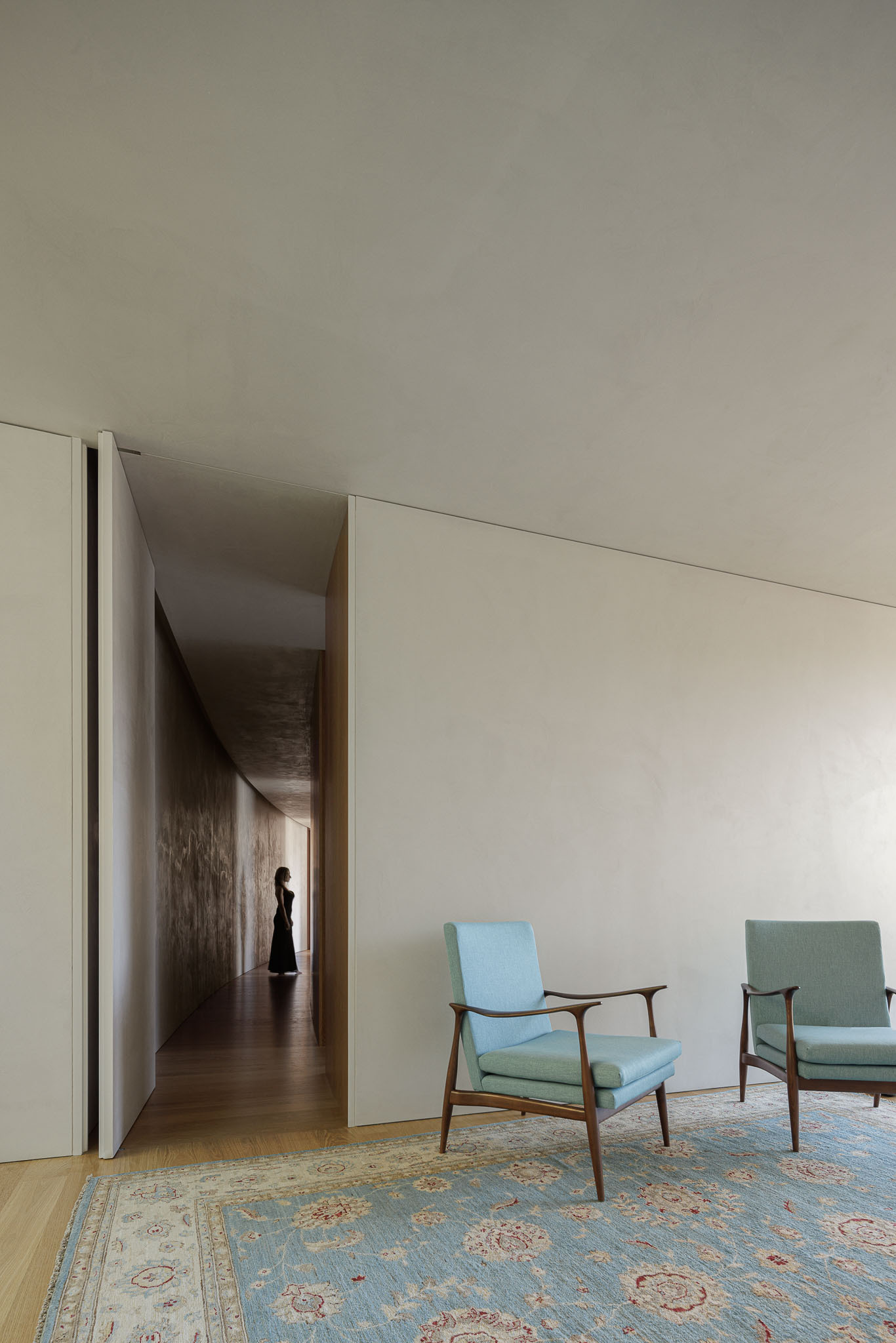 Living room with two midcentury armchairs and doorway opening to corridor where a figure walks