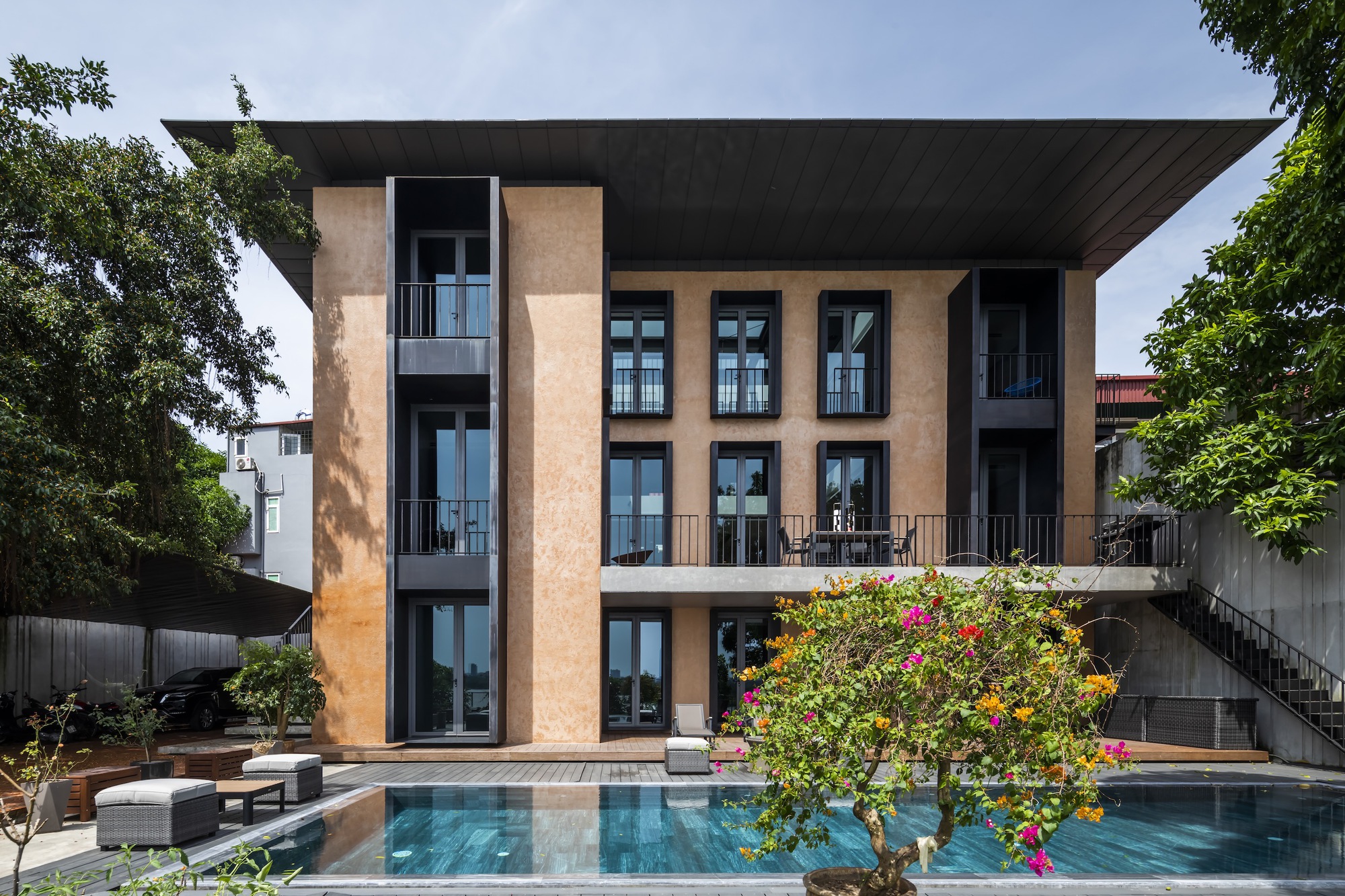 Rear facade with terracotta-textured panels overlooking a swimming pool framed by flowering trees