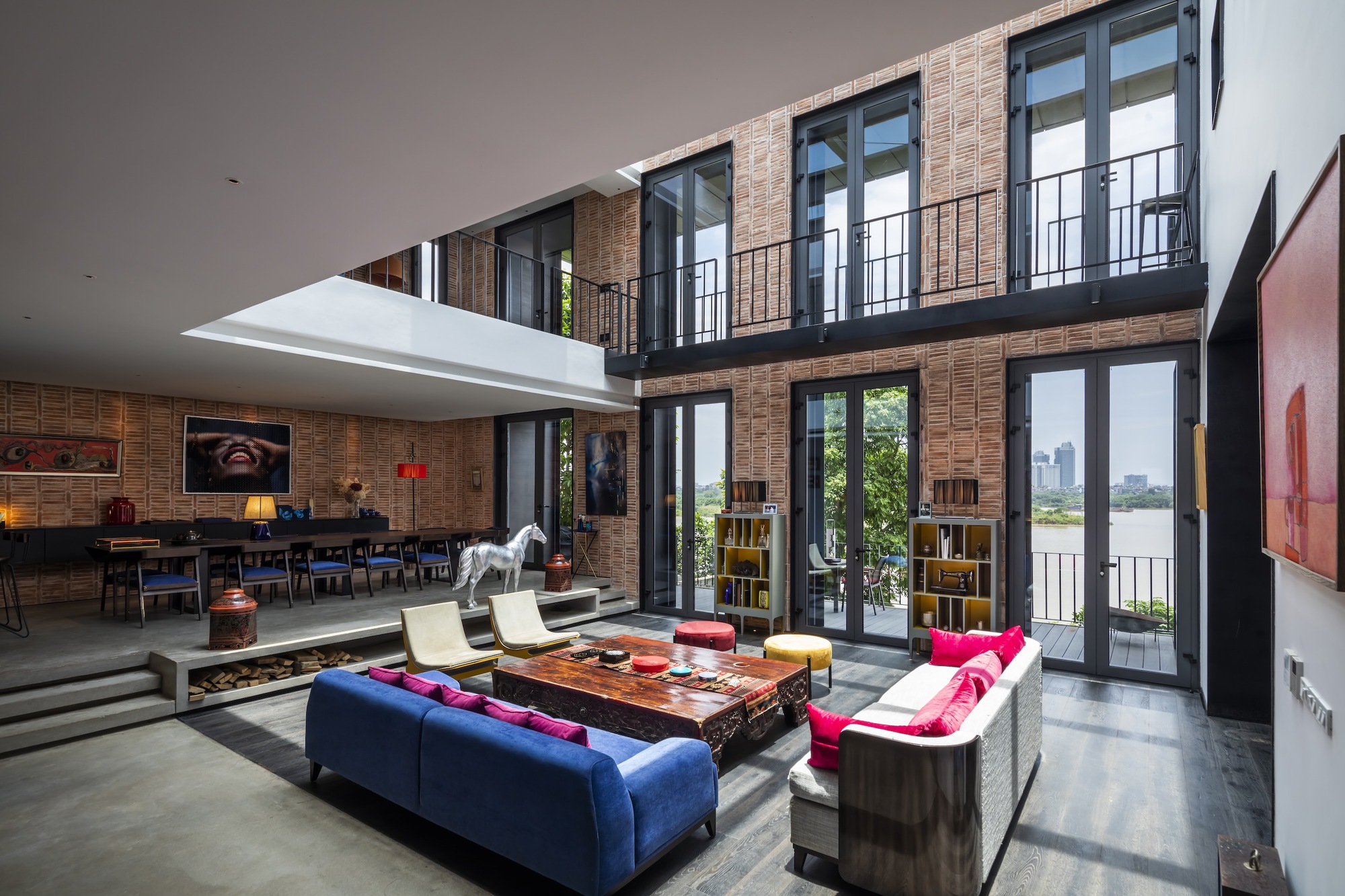 Double-height living room with mezzanine balcony and floor-to-ceiling glass doors opening to greenery