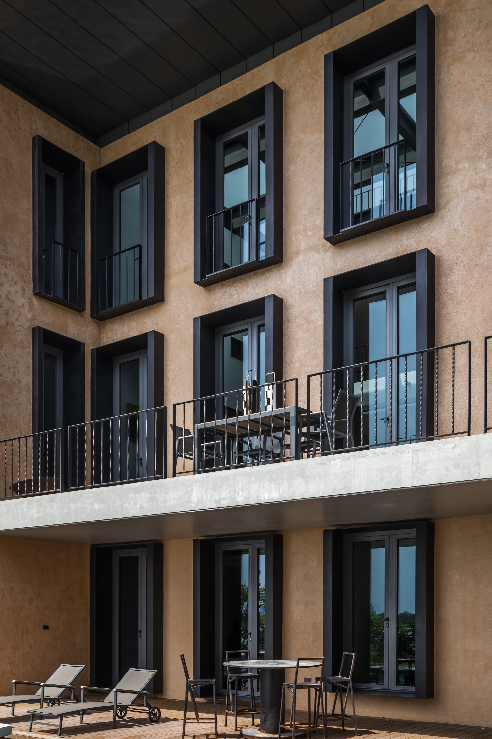 Facade detail showing black-framed windows on terracotta plaster with furnished concrete balcony terrace