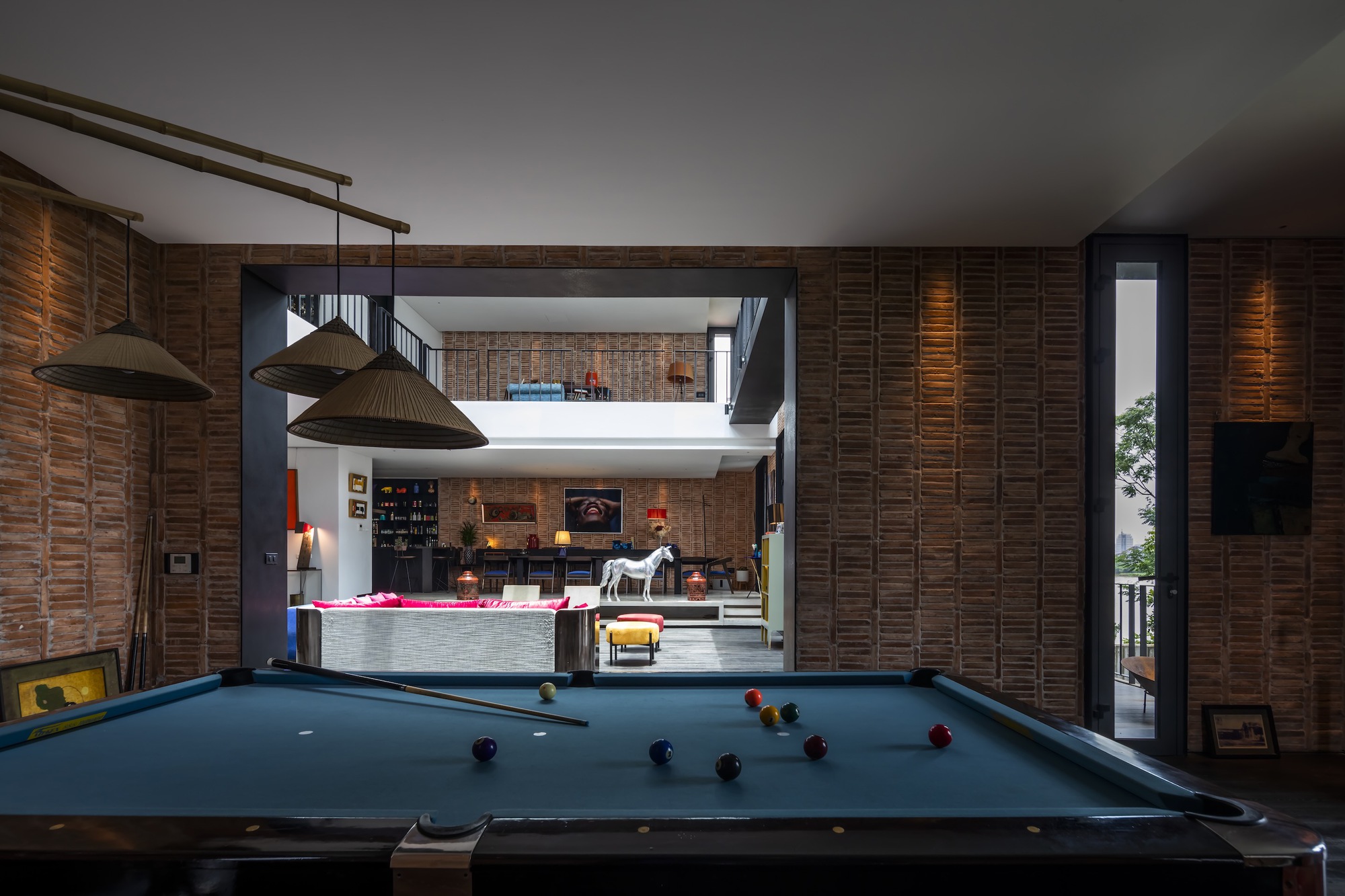 Pool table beneath pendant lights with layered timber slat walls and a double-height void beyond