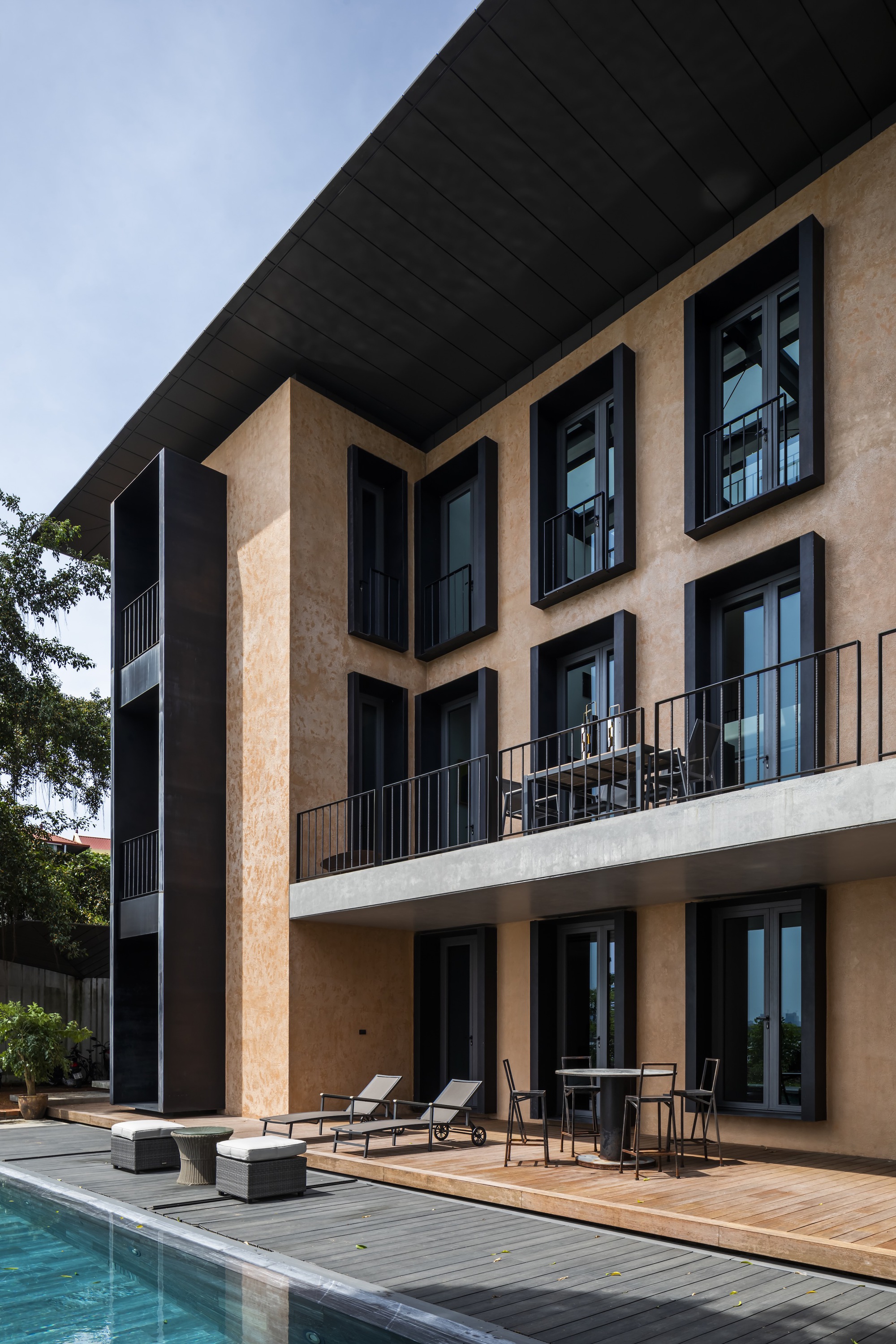 Rear facade with terracotta plaster walls, black-framed windows and timber pool deck beneath a deep overhang