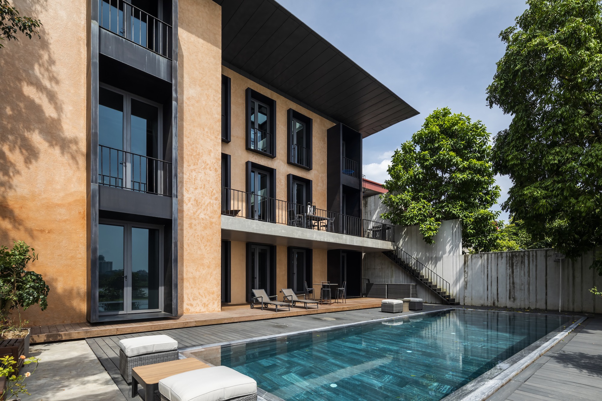 Pool terrace with timber decking, concrete balconies and tree shadows on the terracotta facade