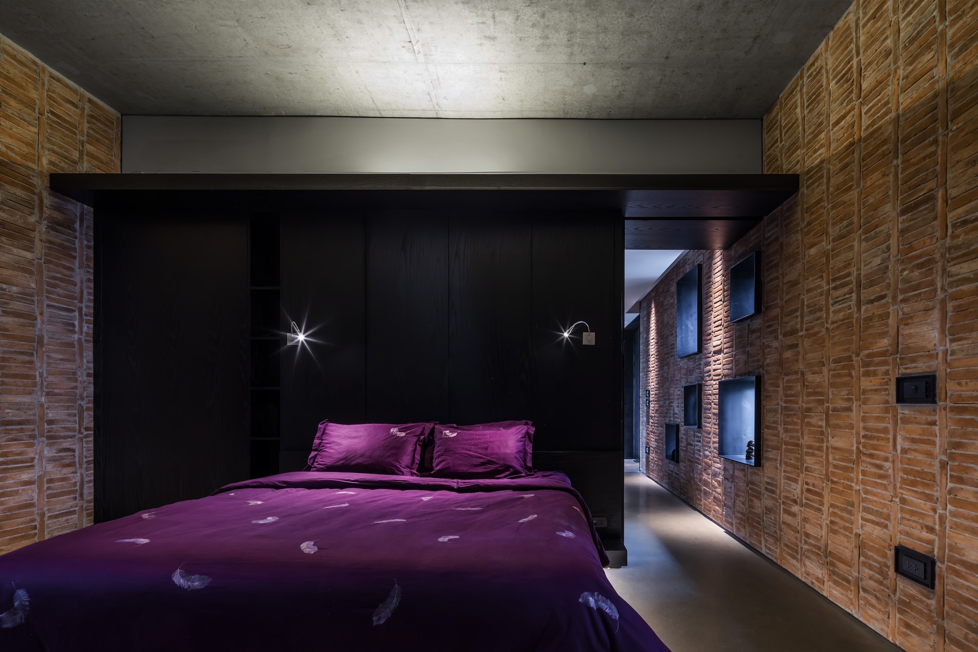 Bedroom with black millwork alcove and brick wall corridor under exposed concrete ceiling