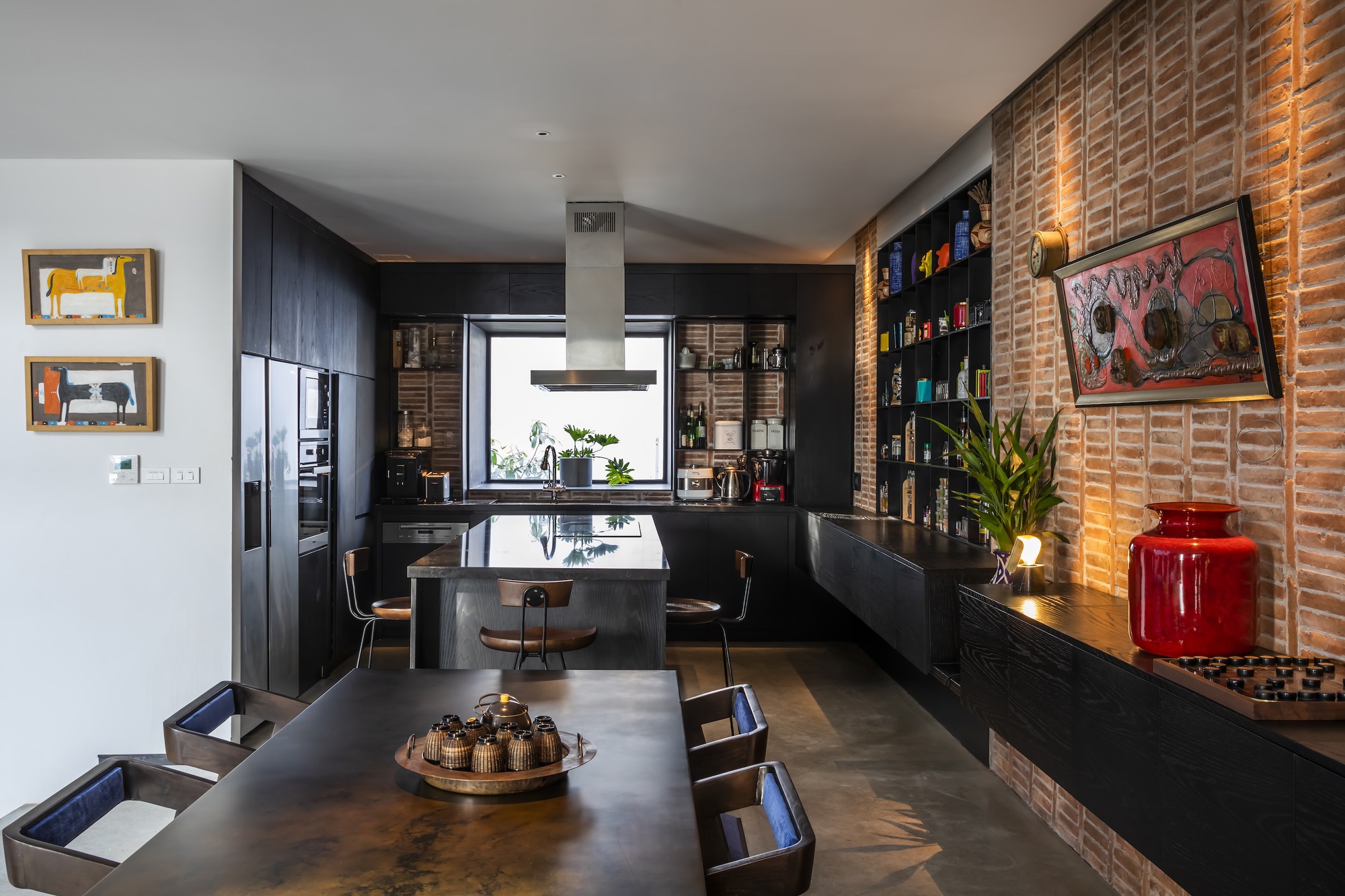 Kitchen and dining area with black cabinetry, a textured terracotta tile wall, and uplighting at dusk
