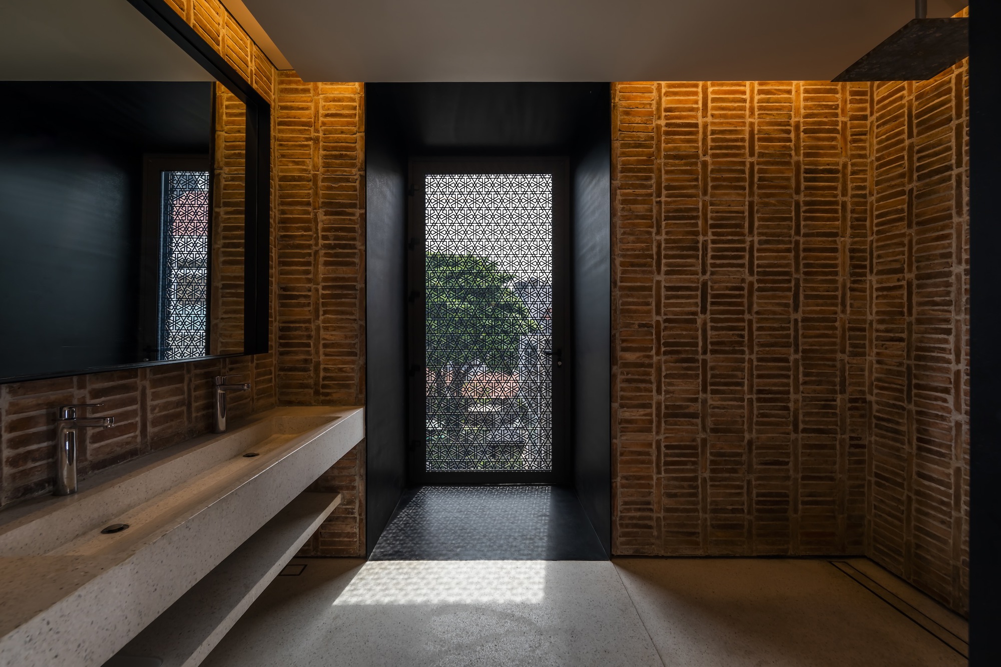 Bathroom corridor with backlit terracotta tile walls framing a perforated metal door opening to greenery