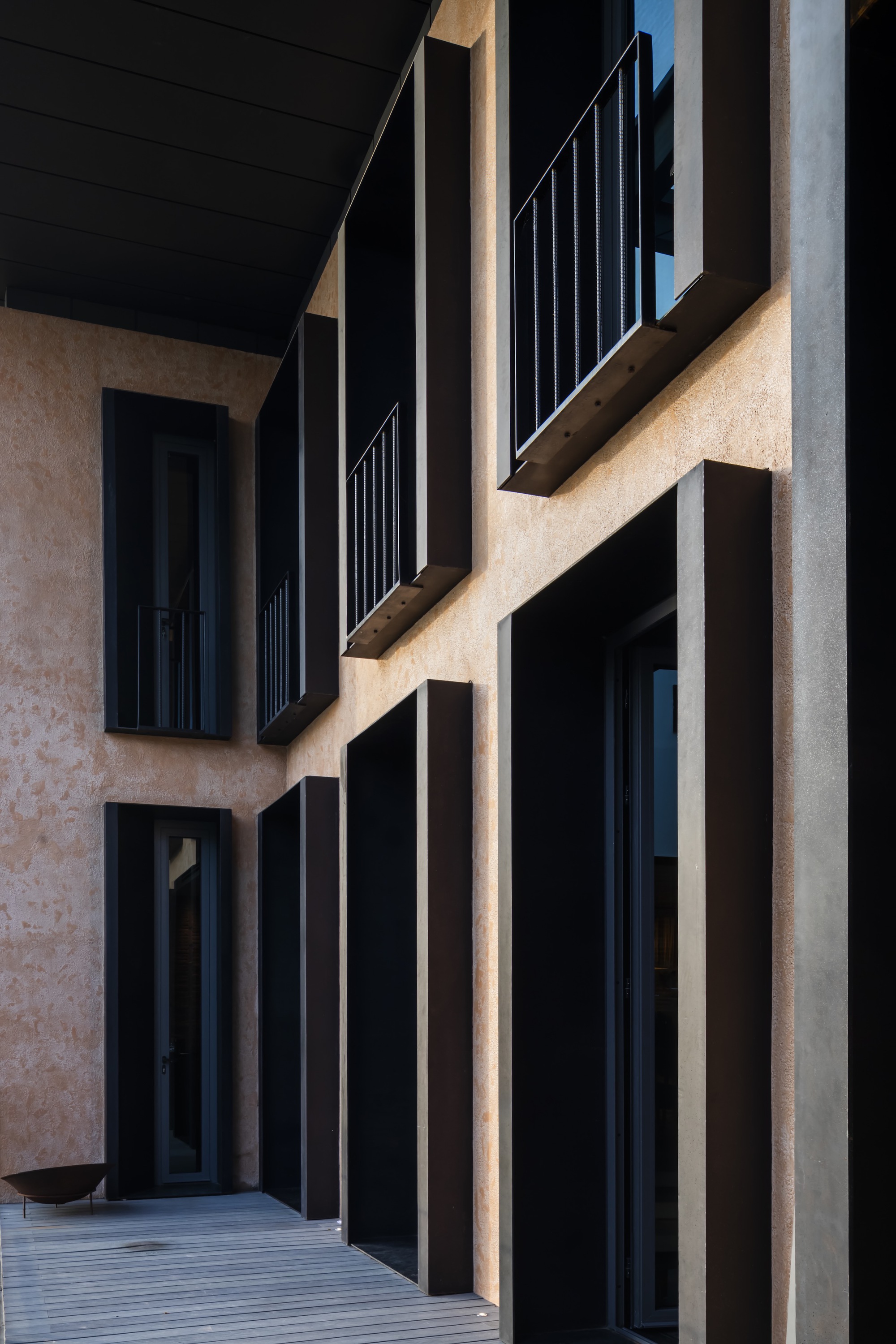Facade detail showing deeply recessed window frames in textured plaster with metal railings and vertical louvers