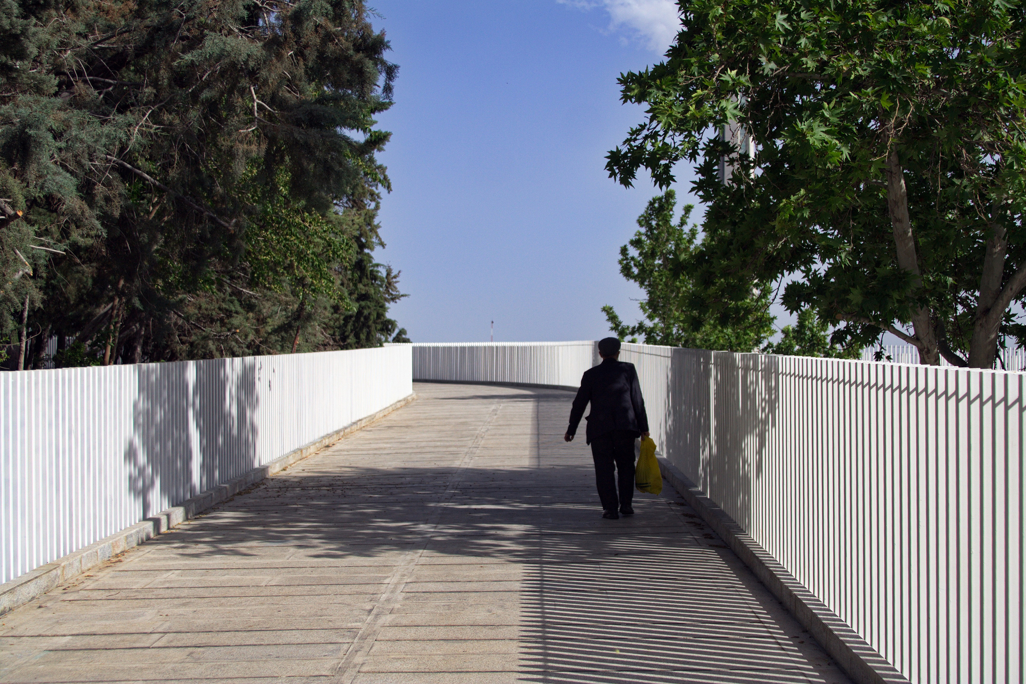 Person walking along the timber-planked pedestrian bridge flanked by white vertical metal screens