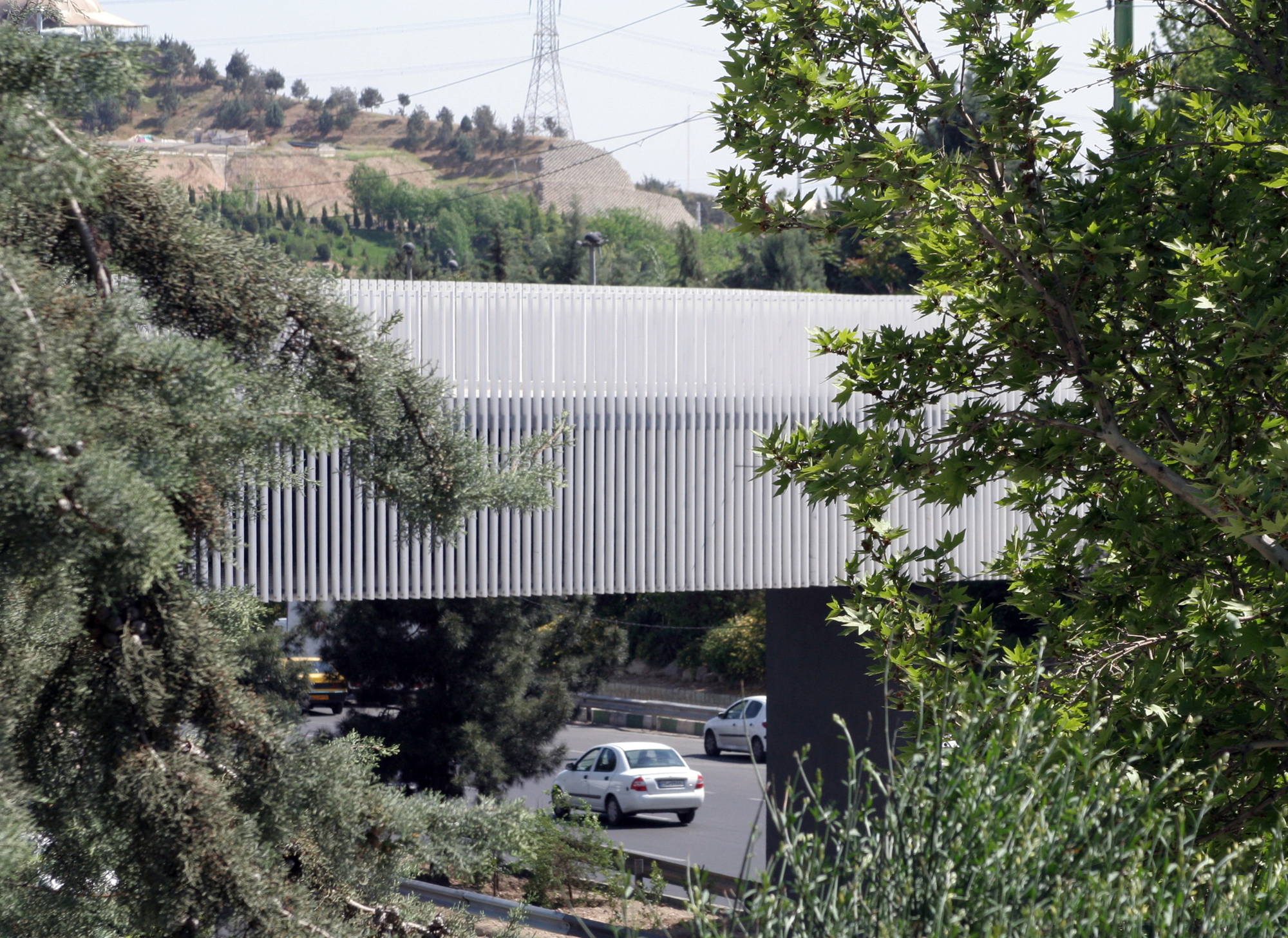 White vertical slat bridge span crossing above a roadway with hillside vegetation framing the view