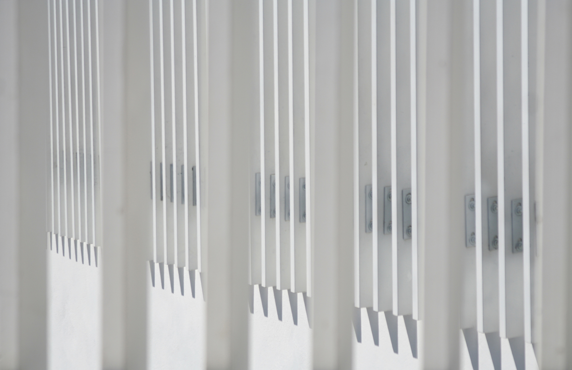 Close-up of white vertical slat screen with sharp shadow lines cast across its stepped profile