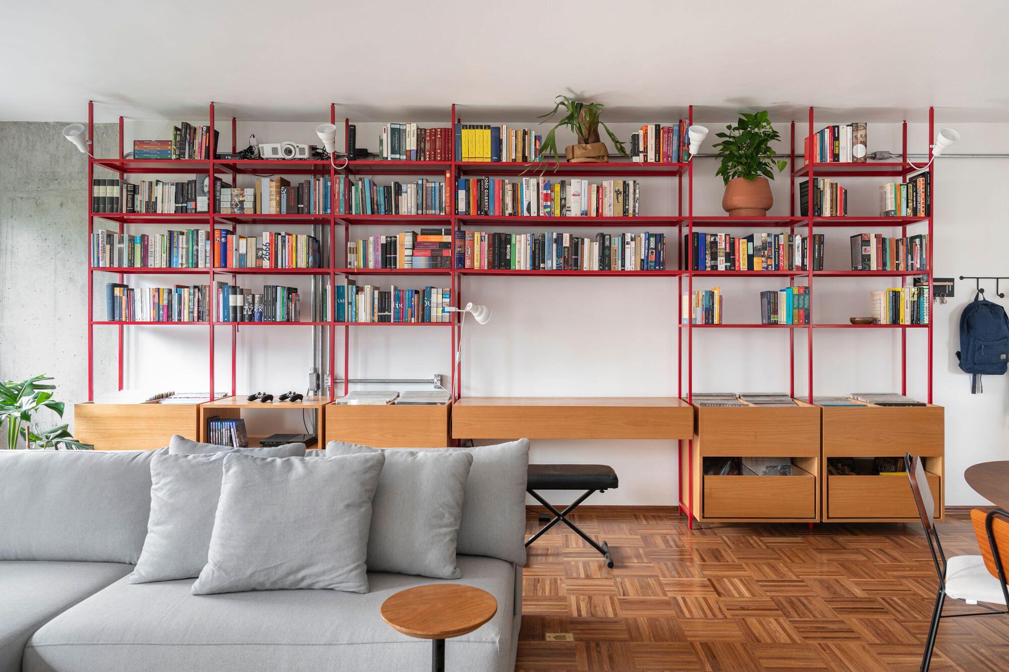 Red steel shelving system with timber desk units spanning a living area with herringbone parquet flooring