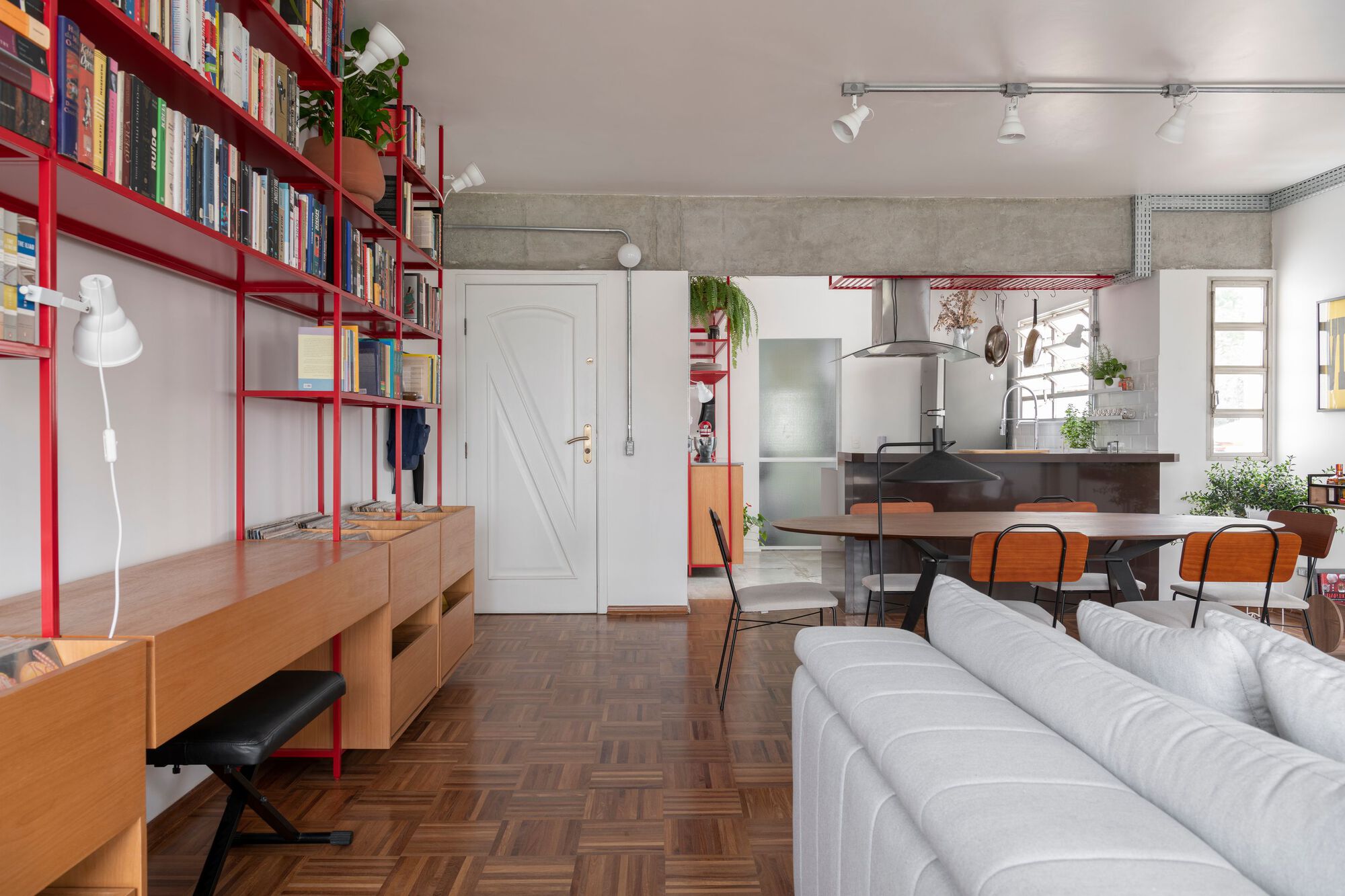 Open-plan living space showing red shelving, white barn door and exposed concrete ceiling beam