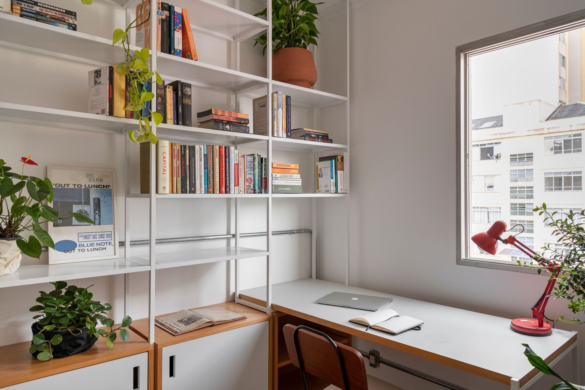 White metal shelving system forming a workspace nook with desk and window overlooking neighboring buildings