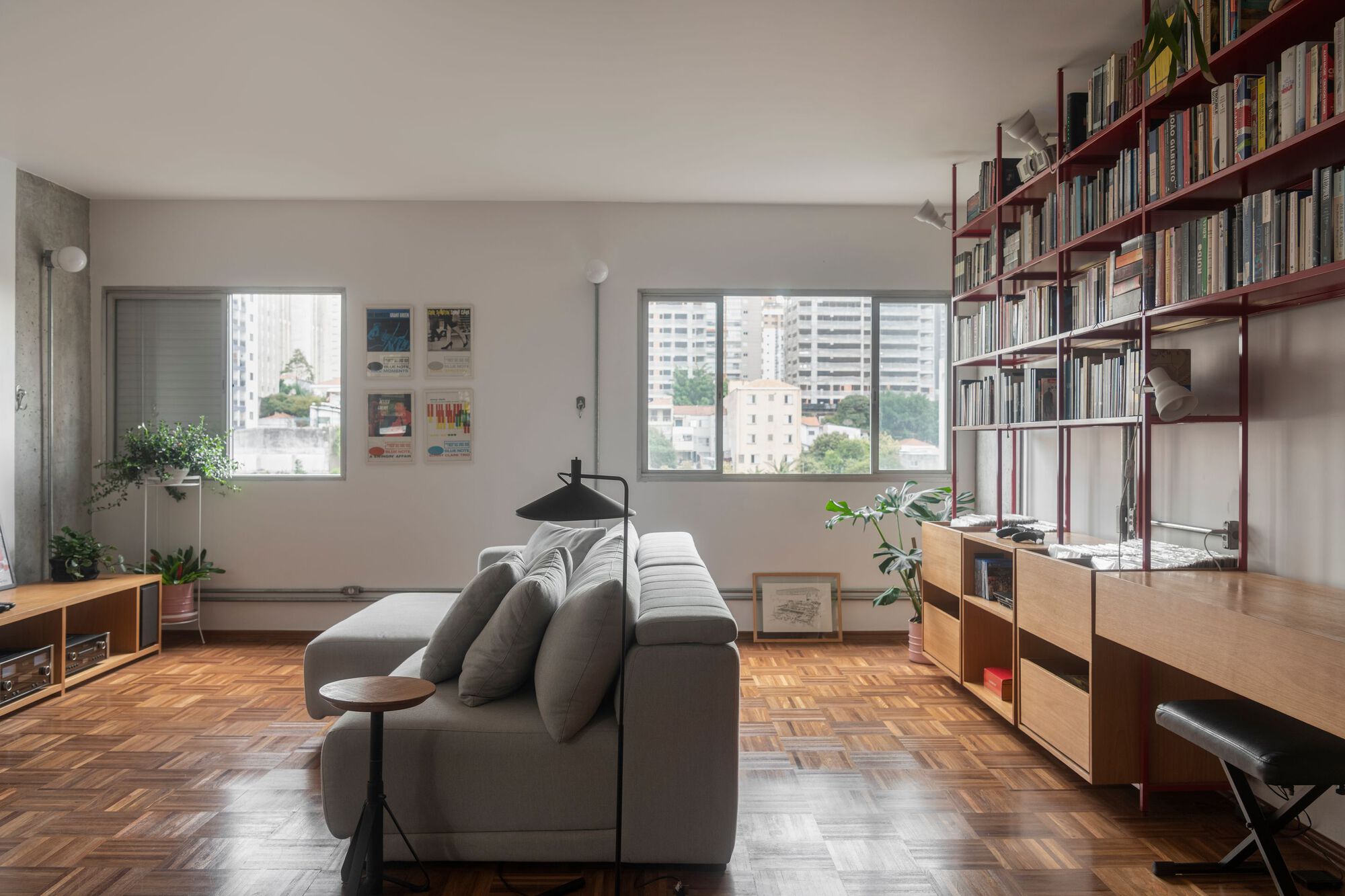 Living room with red shelving unit and windows overlooking neighboring towers