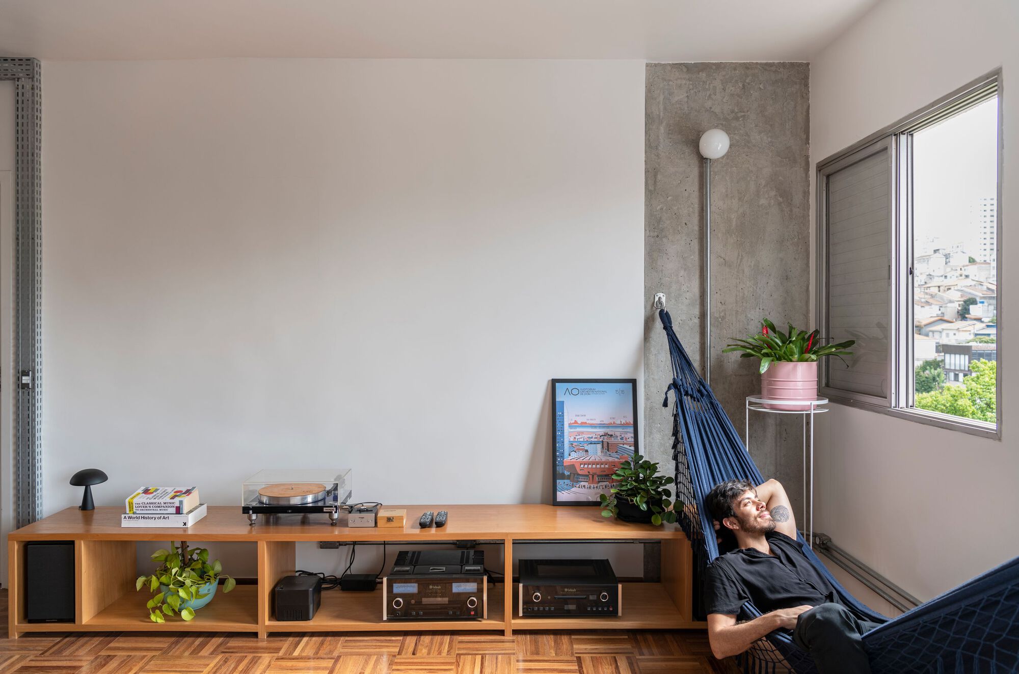 Corner with person reclining in hammock beside window and low storage unit