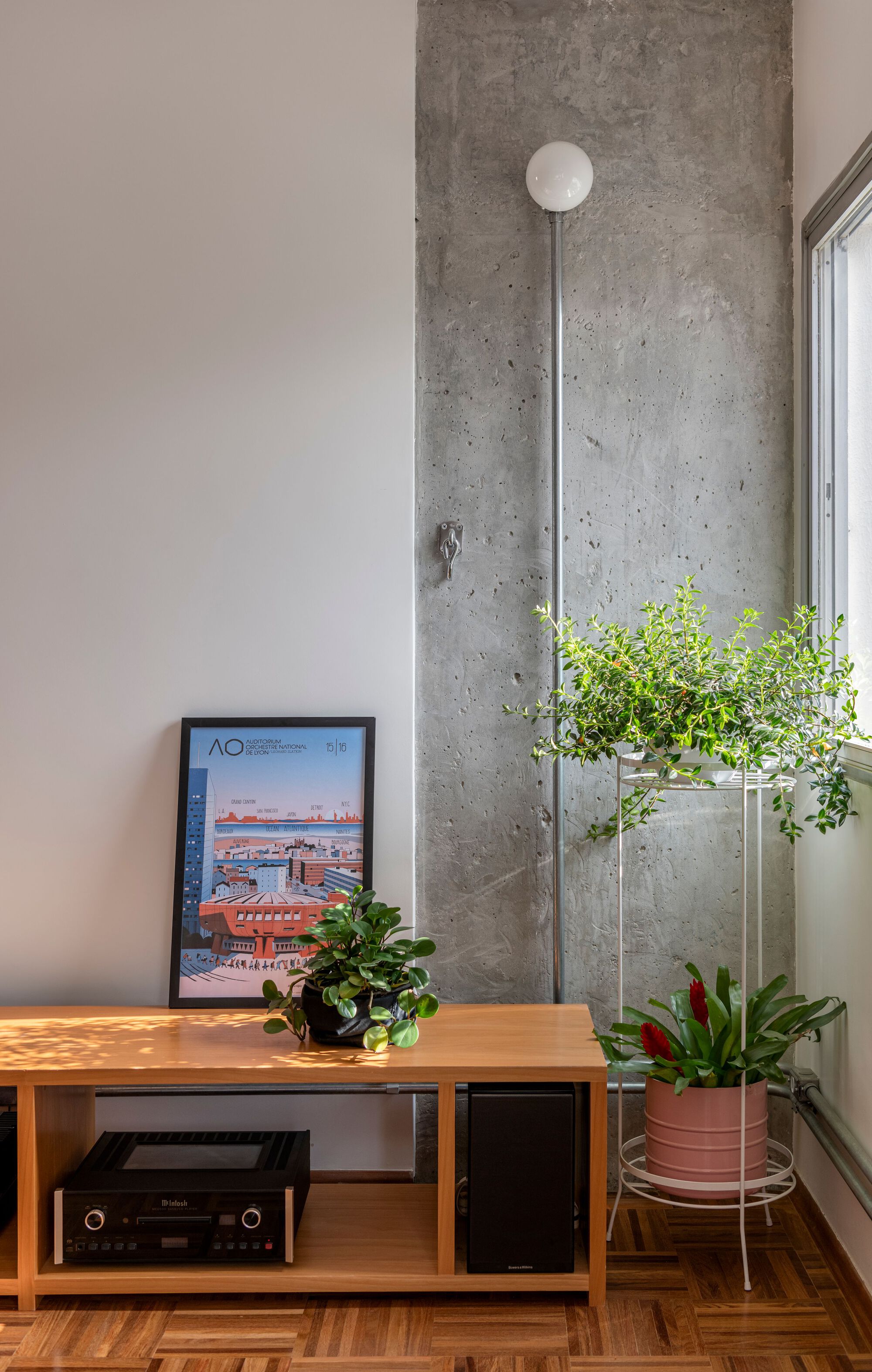Low credenza with audio equipment and potted plants against exposed concrete column with circular conduit mount