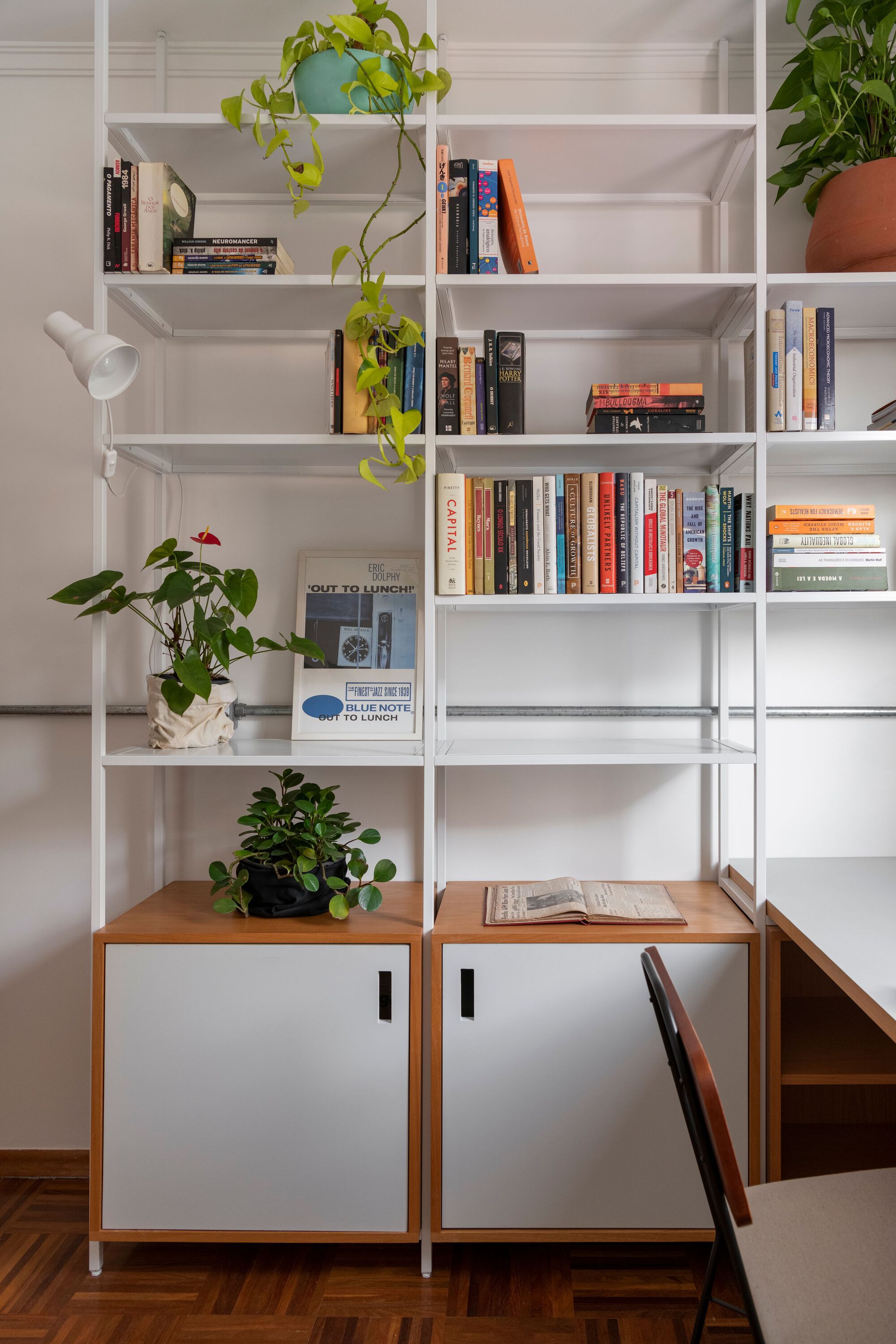 White steel bookshelf with sliding wooden cabinet bases and trailing potted vines on herringbone floor