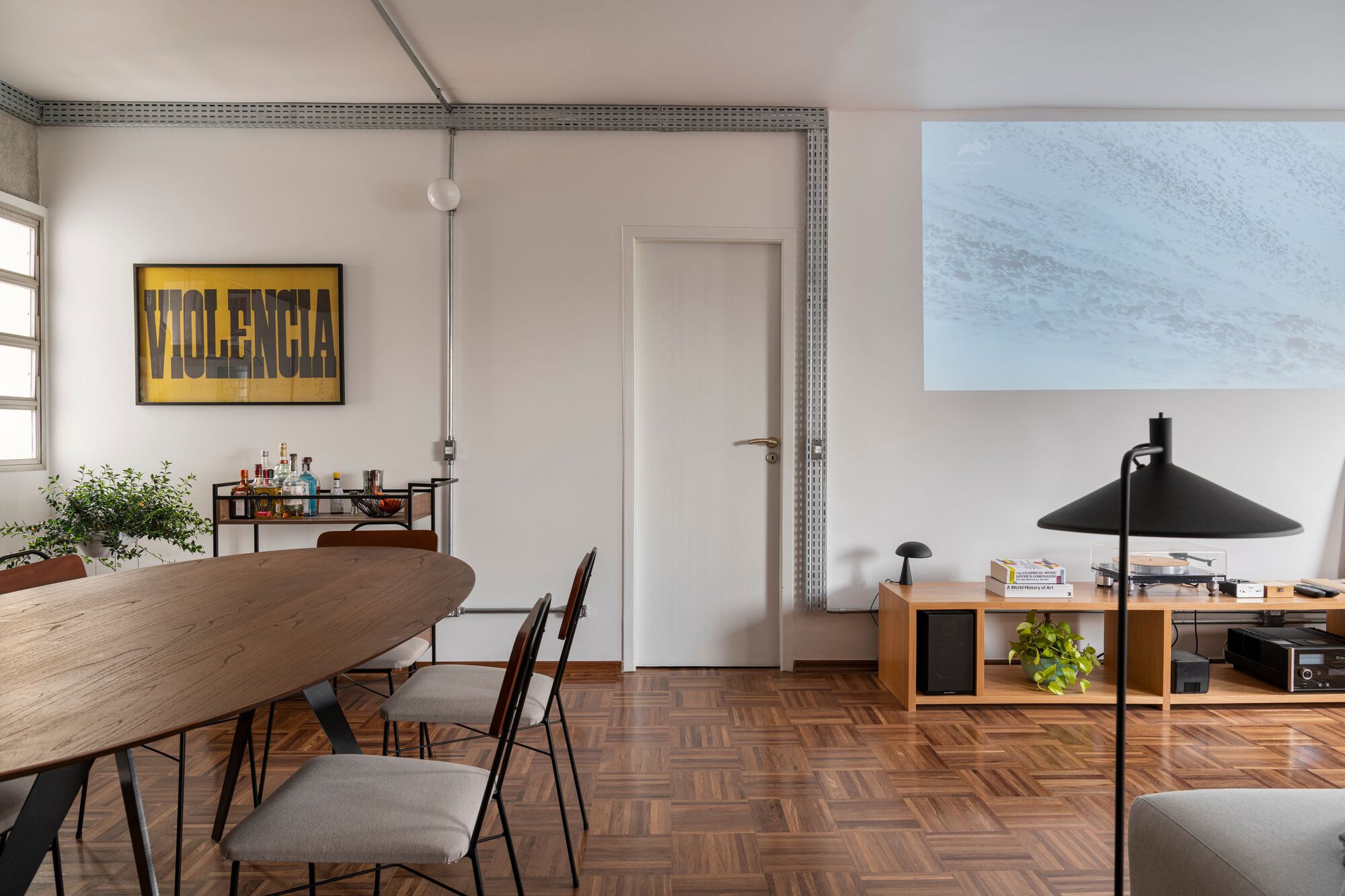 Dining area with round wooden table and parquet flooring beneath exposed conduit and mosaic tile trim