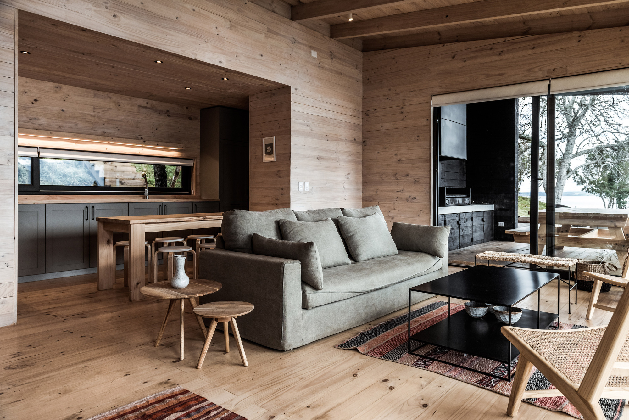 Living space with exposed timber ceiling beams and horizontal plank walls opening to the deck and lake