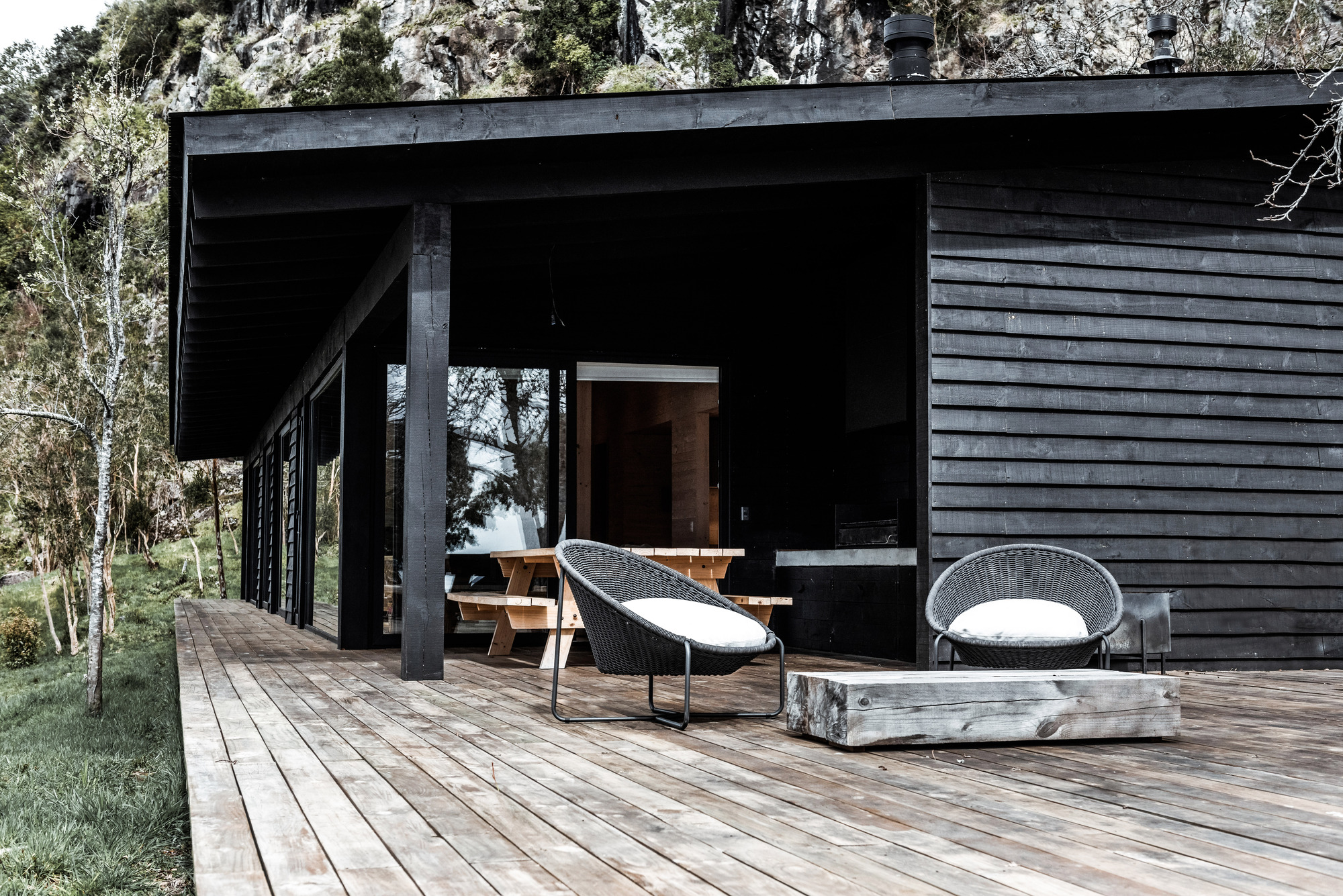 Covered deck with black steel columns and timber furniture beneath the deep eave and horizontal cladding