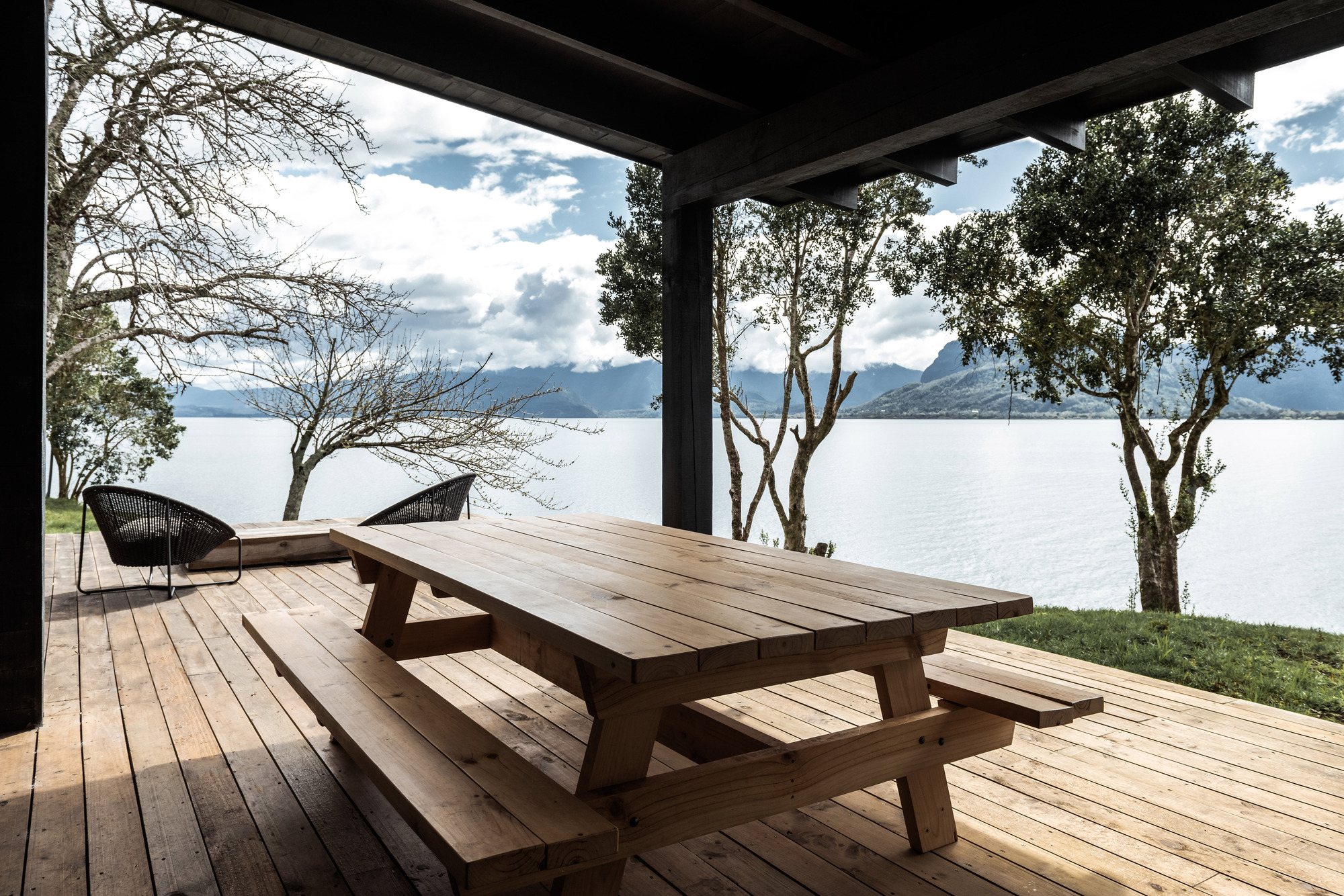 Timber picnic table under the porch roof framing views of the lake and scattered trees beyond