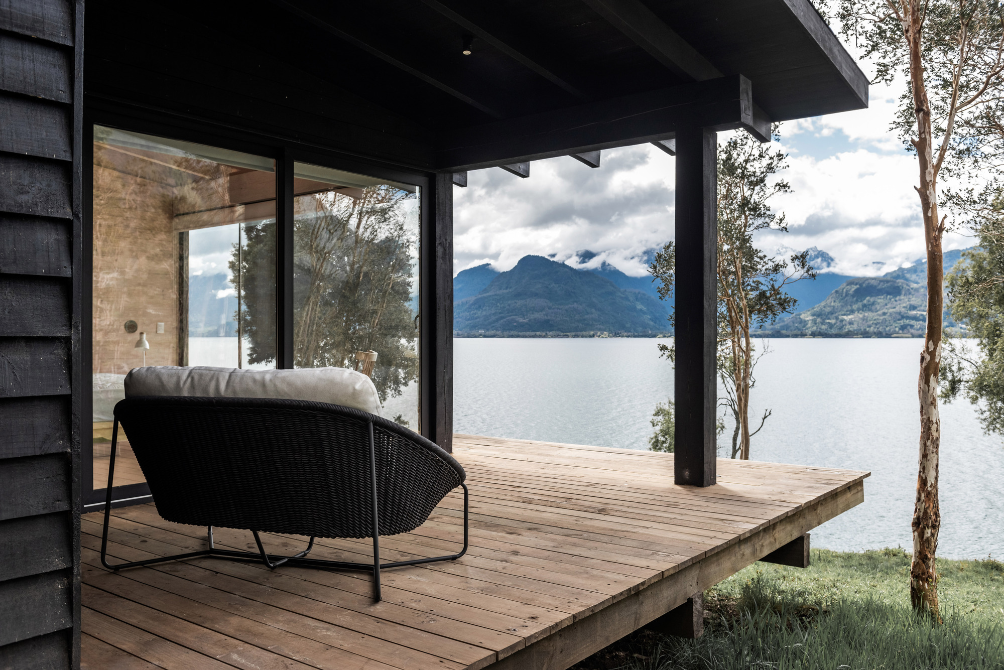 Covered timber deck with black columns and exposed beams overlooking a lake and distant mountains