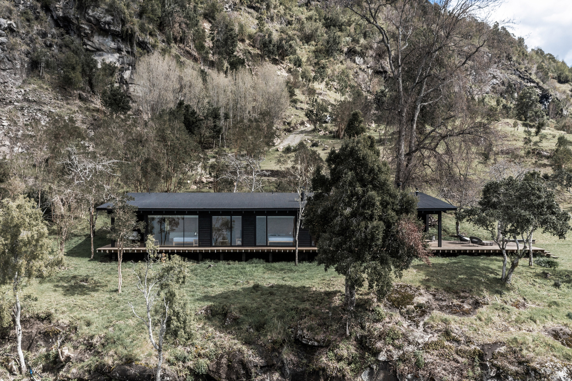 Elevated single-story volume with dark cladding and timber deck set into a sloping hillside