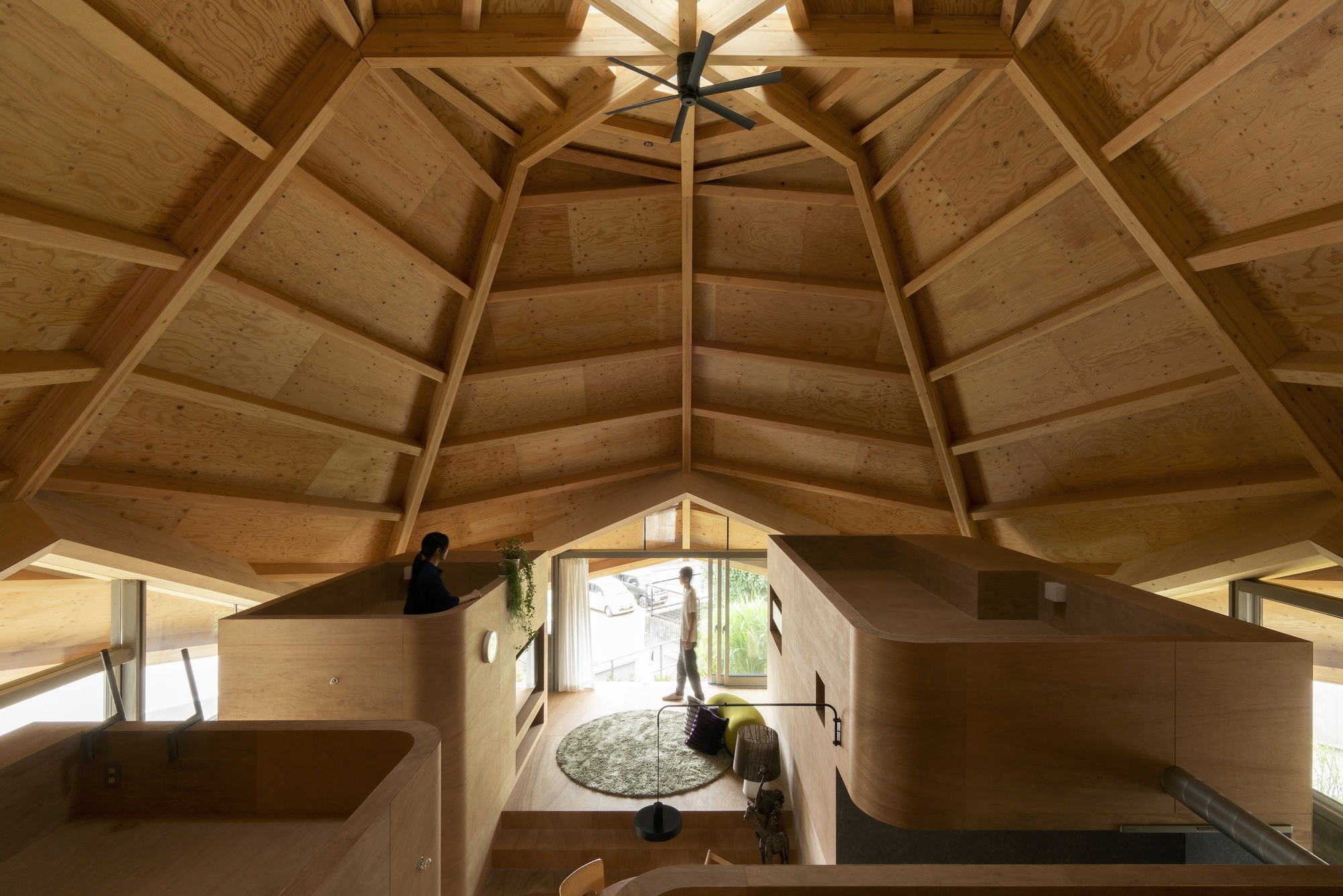Upward view of the polygonal timber ceiling with exposed beams and central skylight above plywood room modules