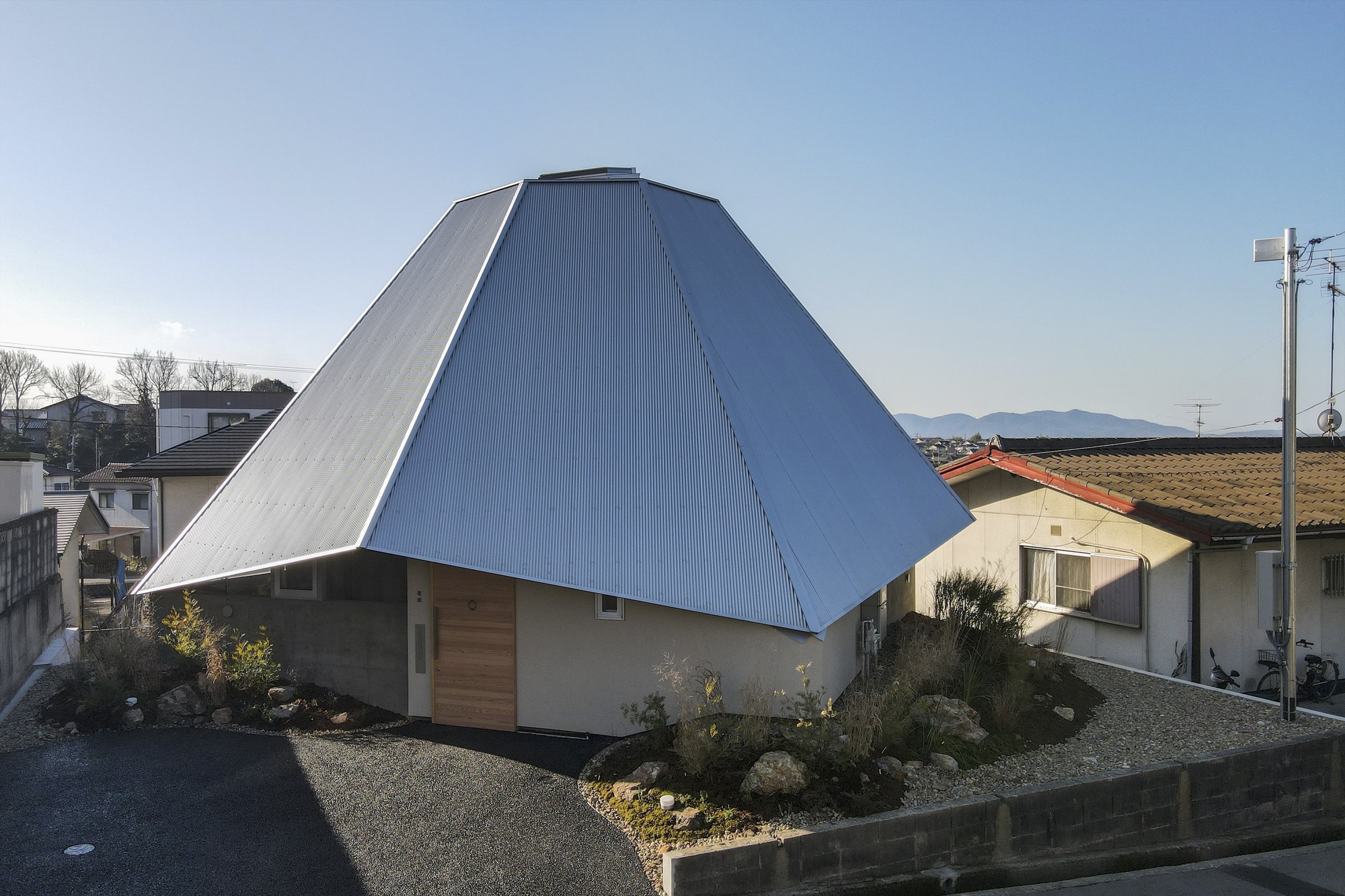 Exterior view of the pyramidal metal roof over plywood walls with a landscaped gravel yard