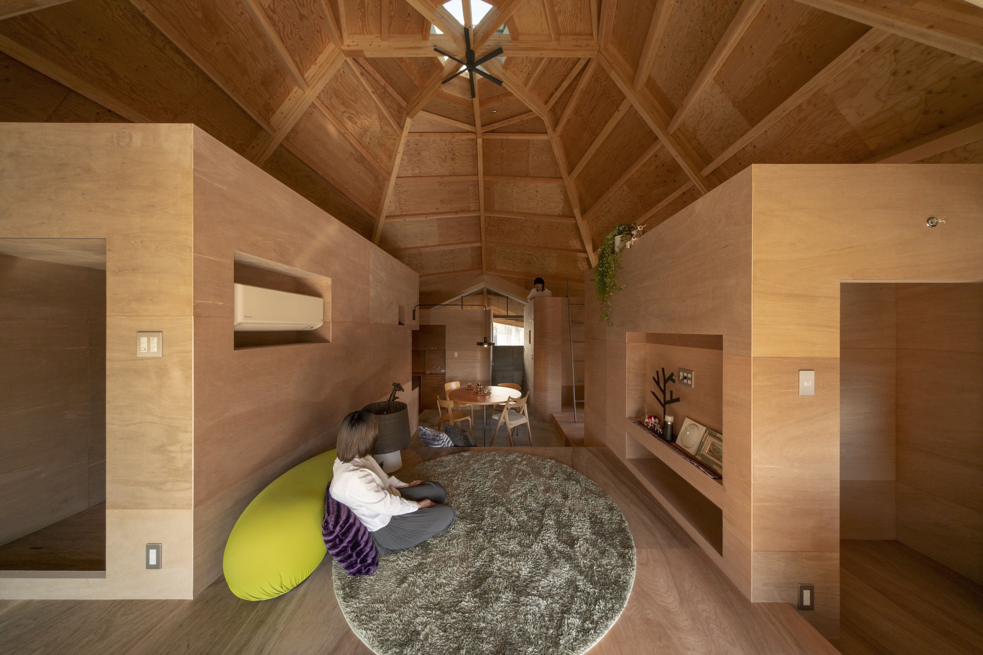 Interior showing plywood room volumes with recessed niches and a circular rug under the timber ceiling