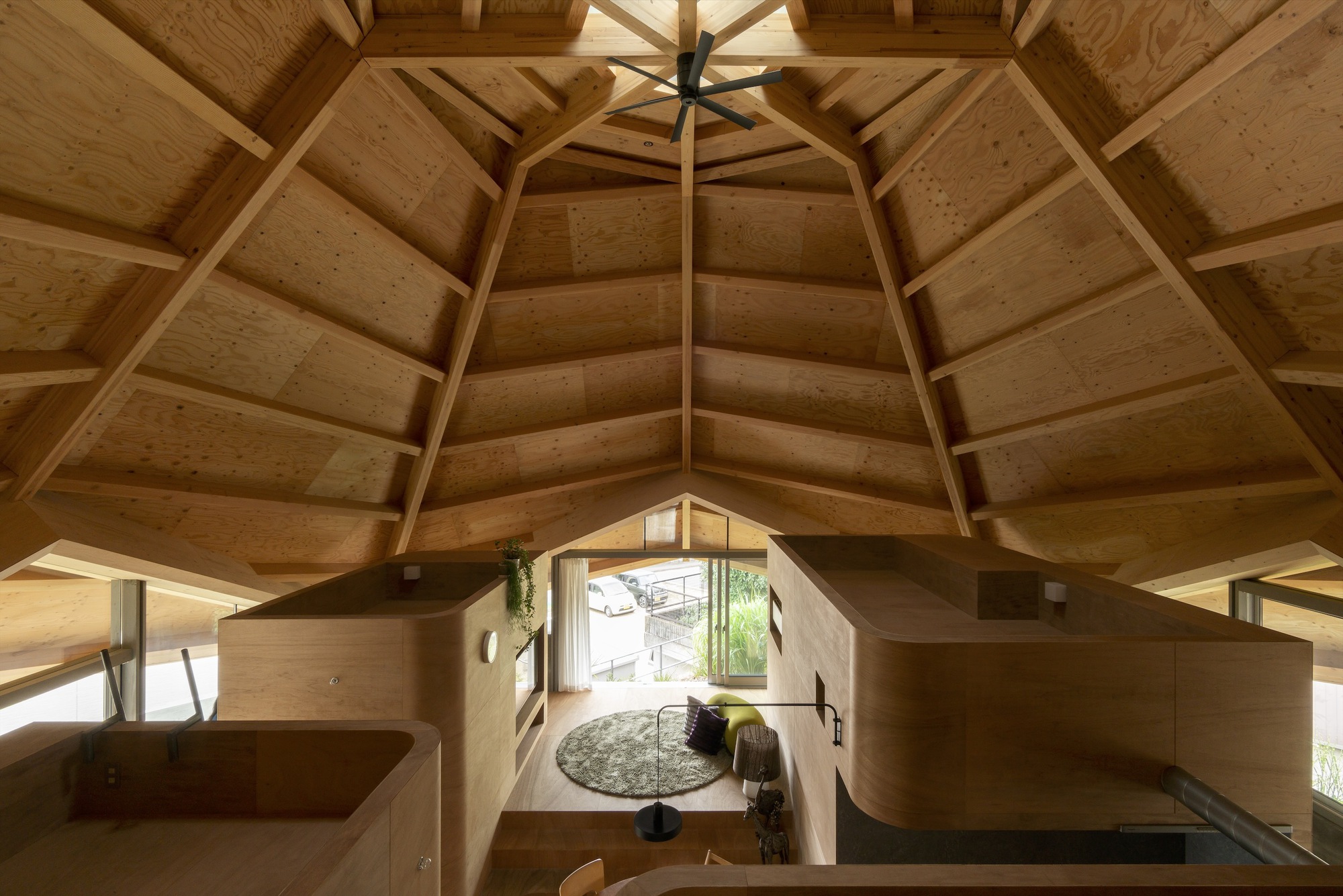 View down into the plywood interior volumes from an upper platform beneath the faceted timber ceiling