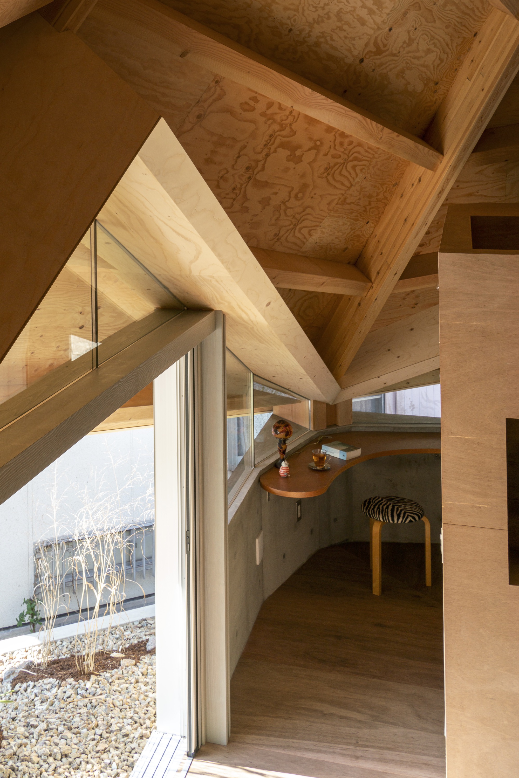 Interior view of plywood-clad volumes beneath exposed timber roof rafters with a person seated at a curved alcove