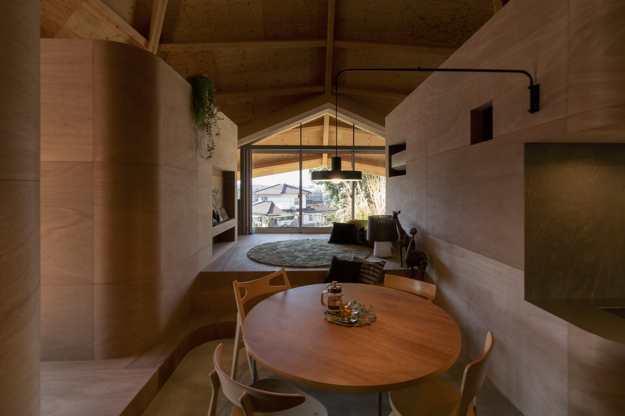 Dining area with round timber table beneath a gabled window framing a view of neighboring rooftops