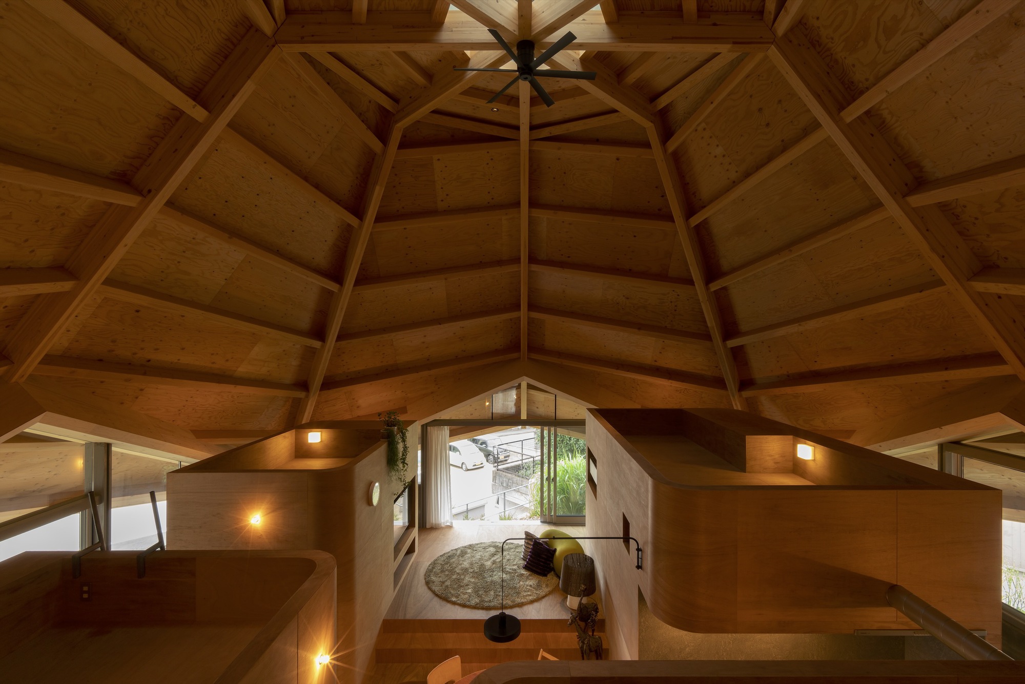 Overhead view into the plywood-lined living space illuminated by warm sconces at dusk