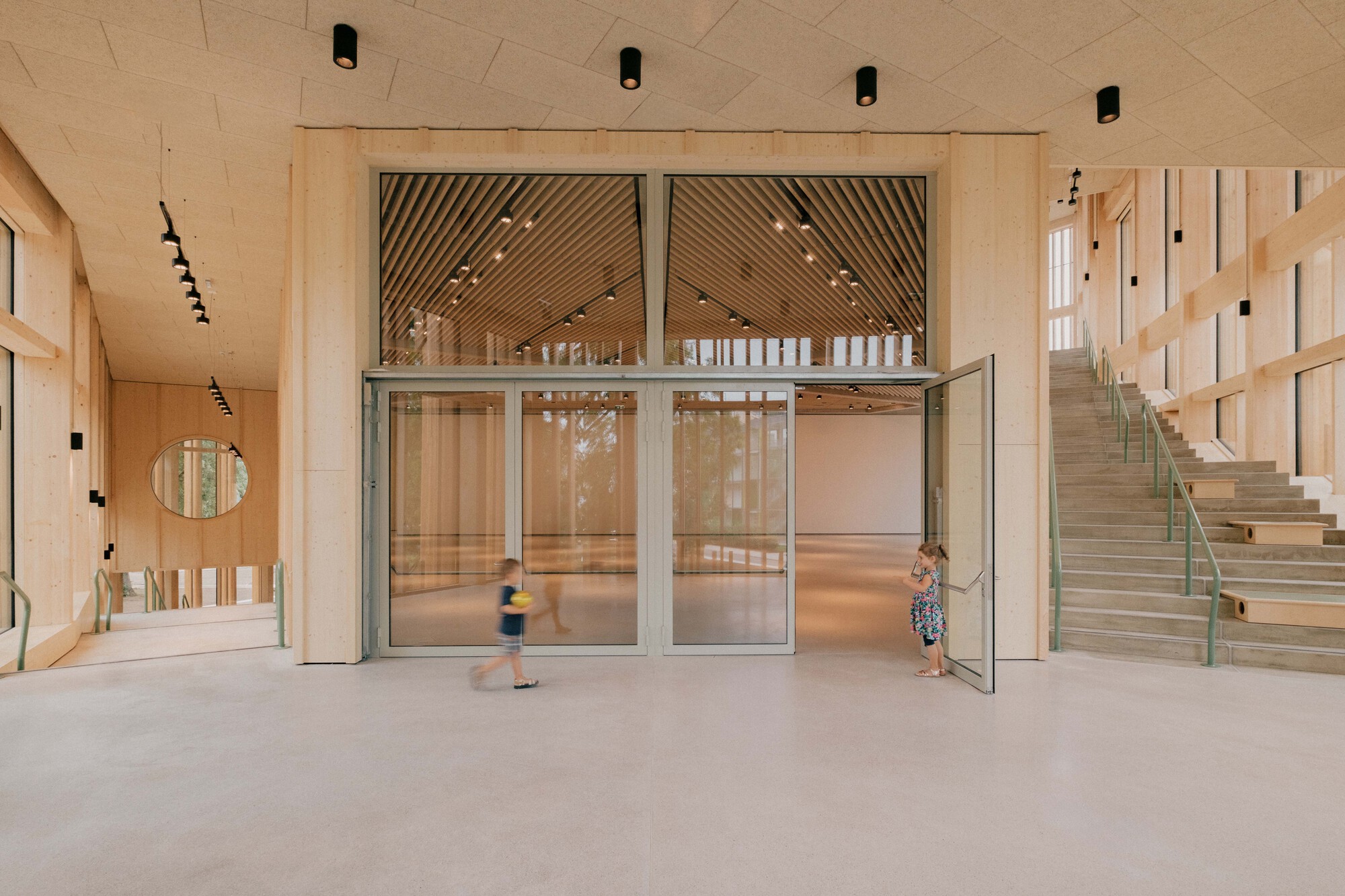 Ground floor lobby with glass doors and children moving through the polished concrete space