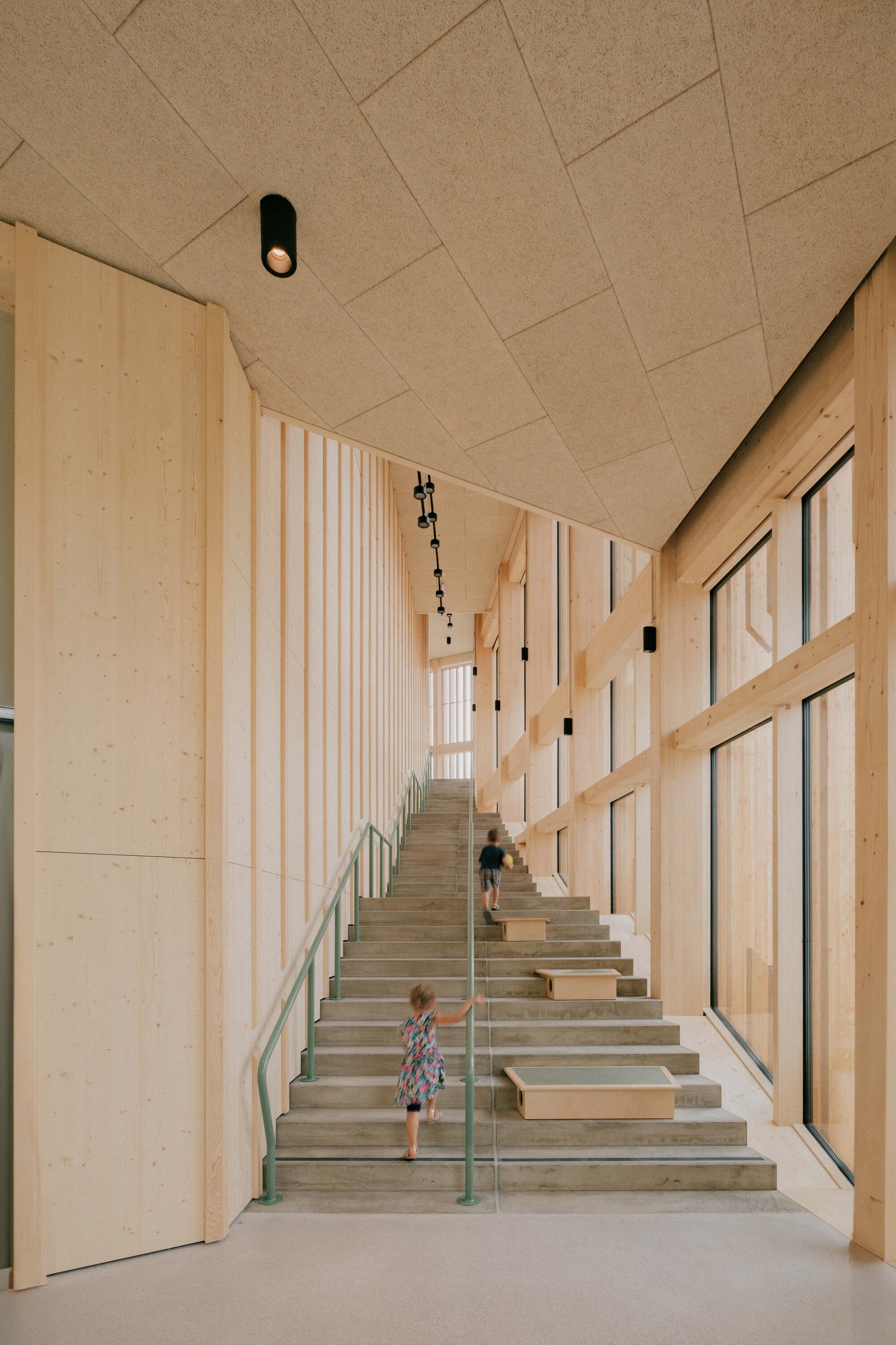 Timber-lined stairwell with diagonal acoustic ceiling panels and child descending the steps