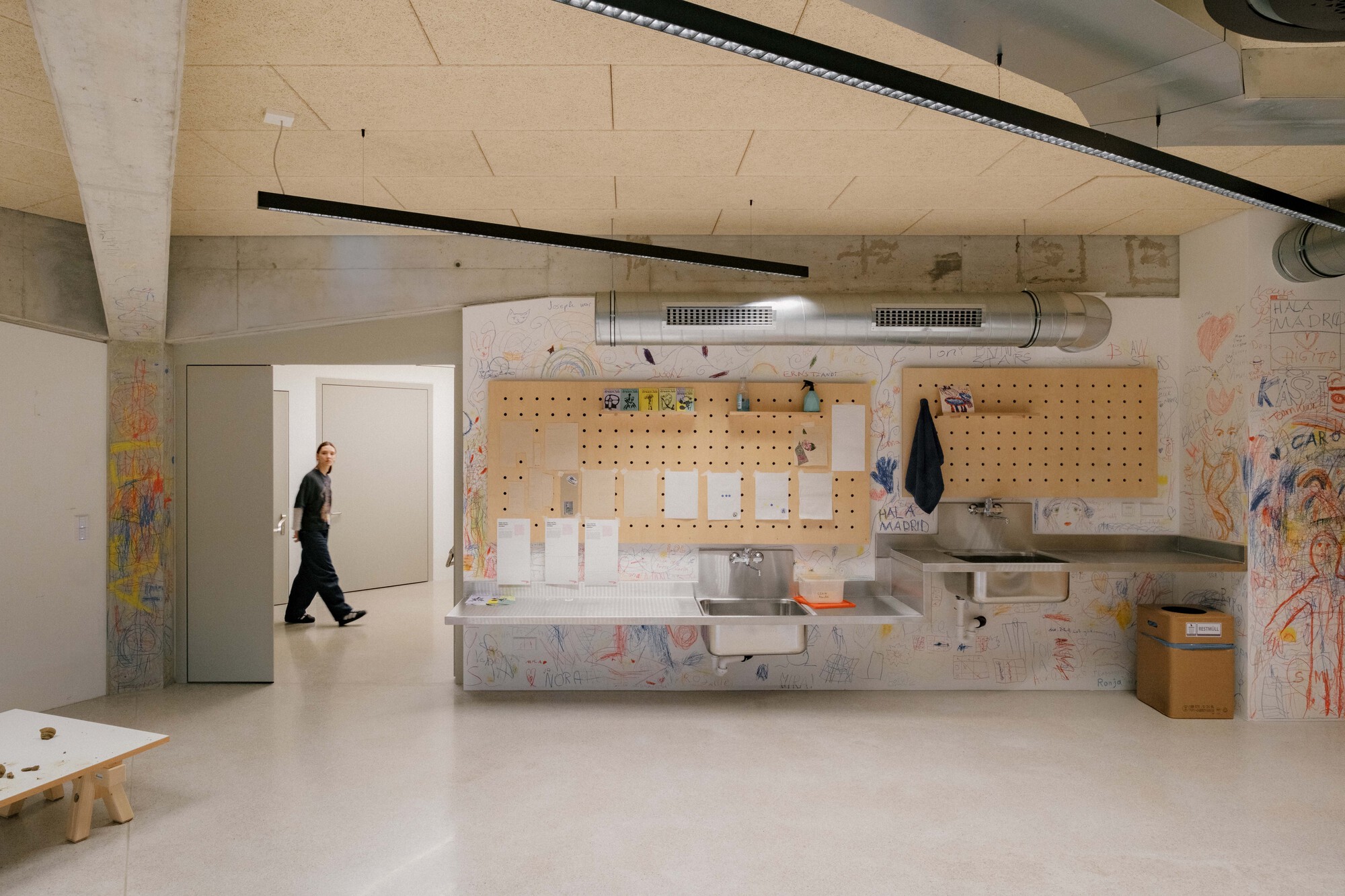 Children's washroom with perforated plywood pegboard and exposed concrete ceiling beams