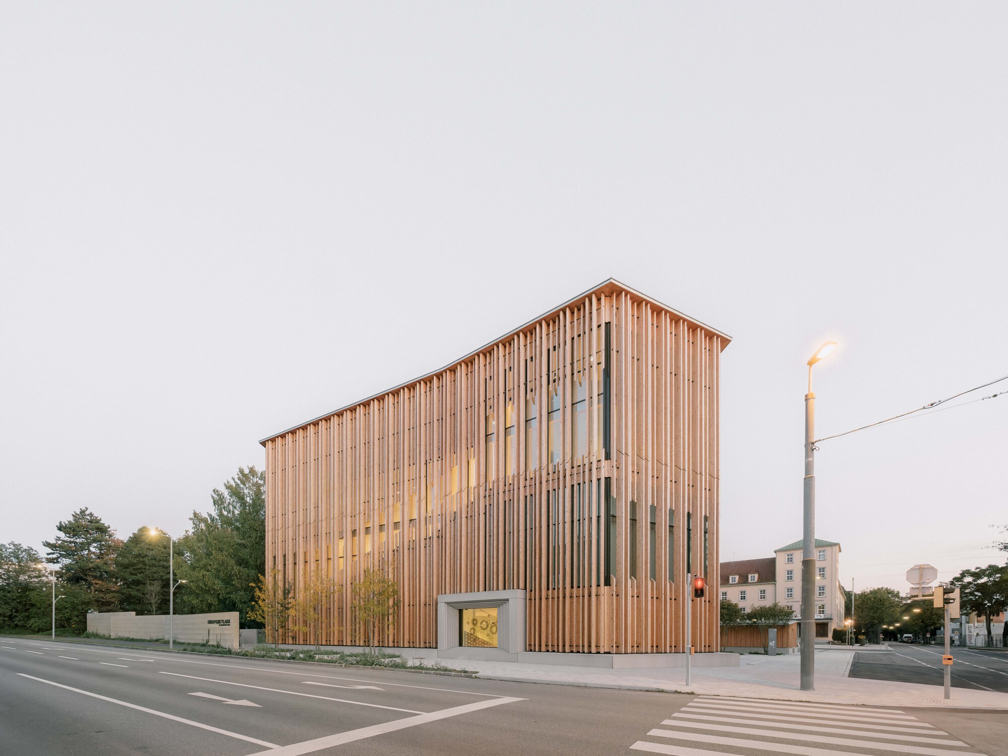 Corner elevation showing the slatted timber box facade at dusk with internal lights glowing