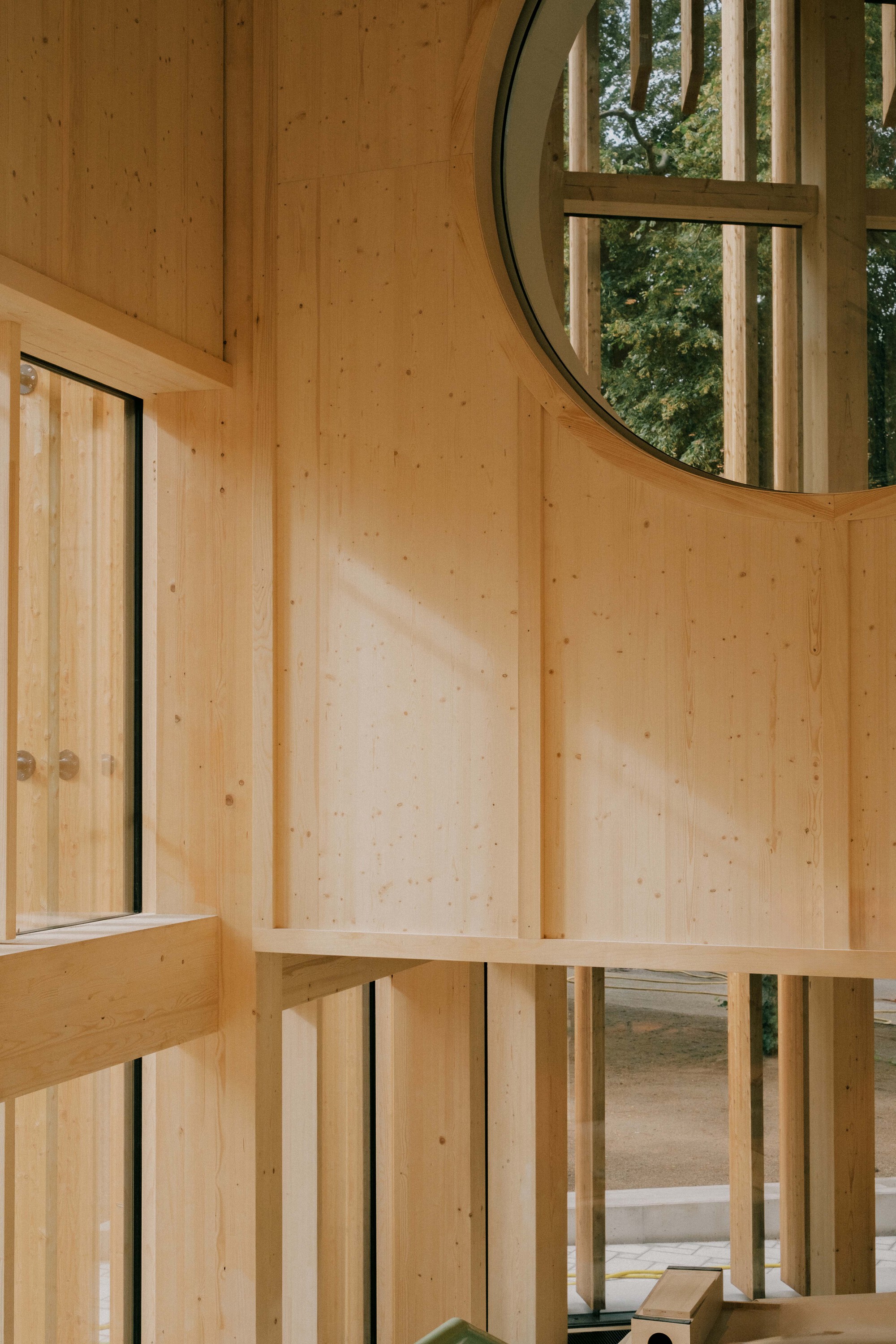 Double-height timber wall with circular window and framed stairwell opening in warm afternoon light