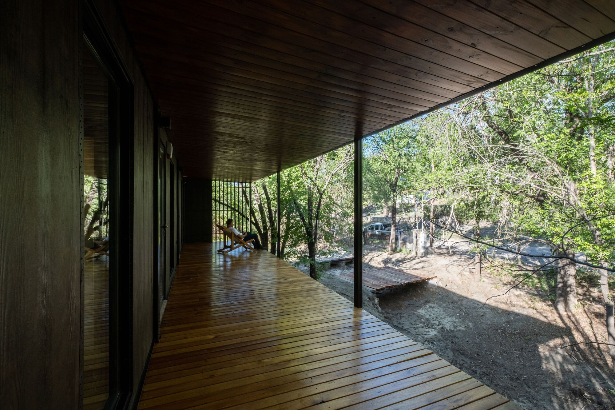 Covered timber deck with sloped ceiling and full-height glazing overlooking rocky woodland terrain