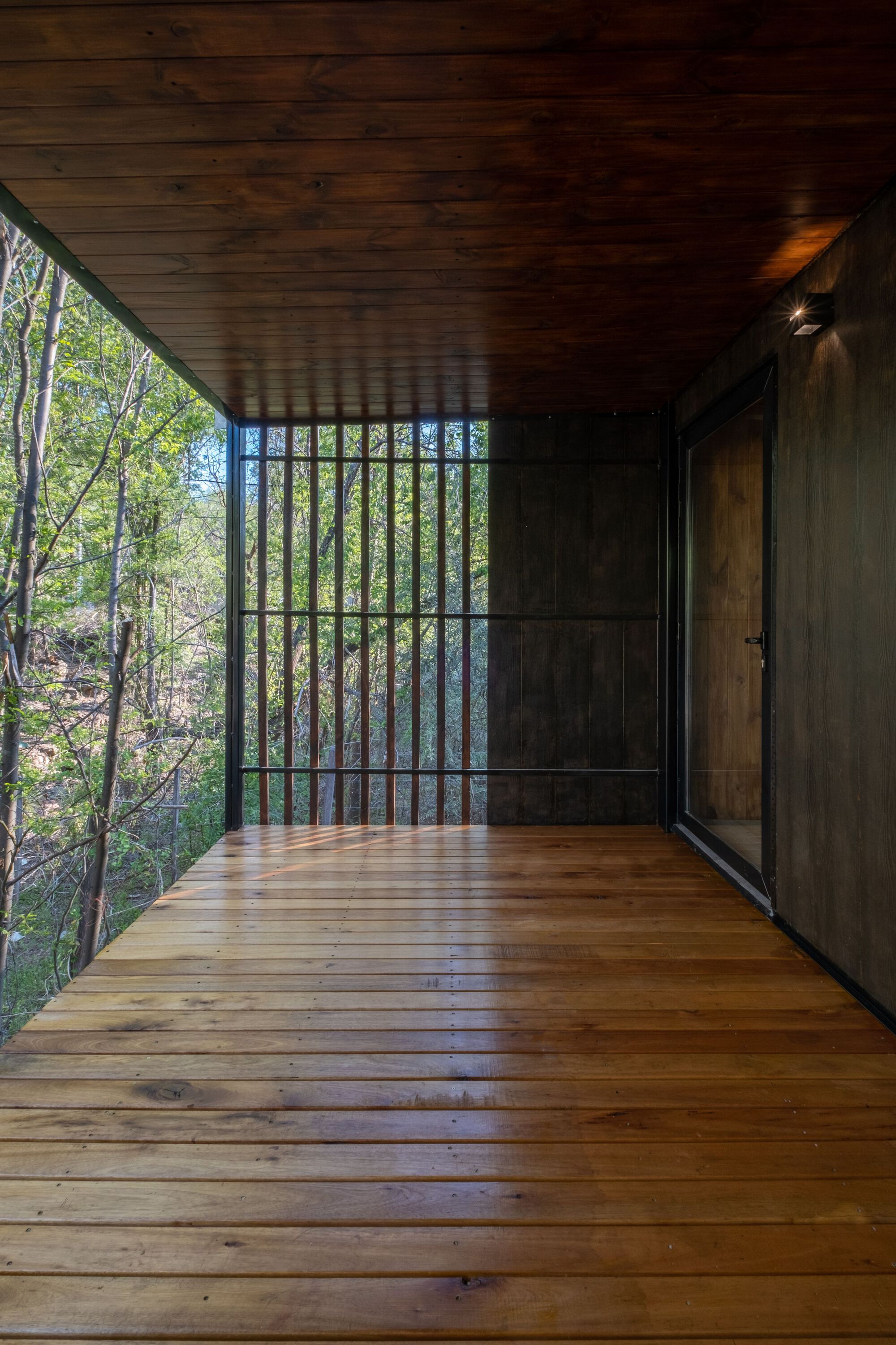 Interior corner of the deck showing vertical metal grille and timber ceiling with dappled afternoon light
