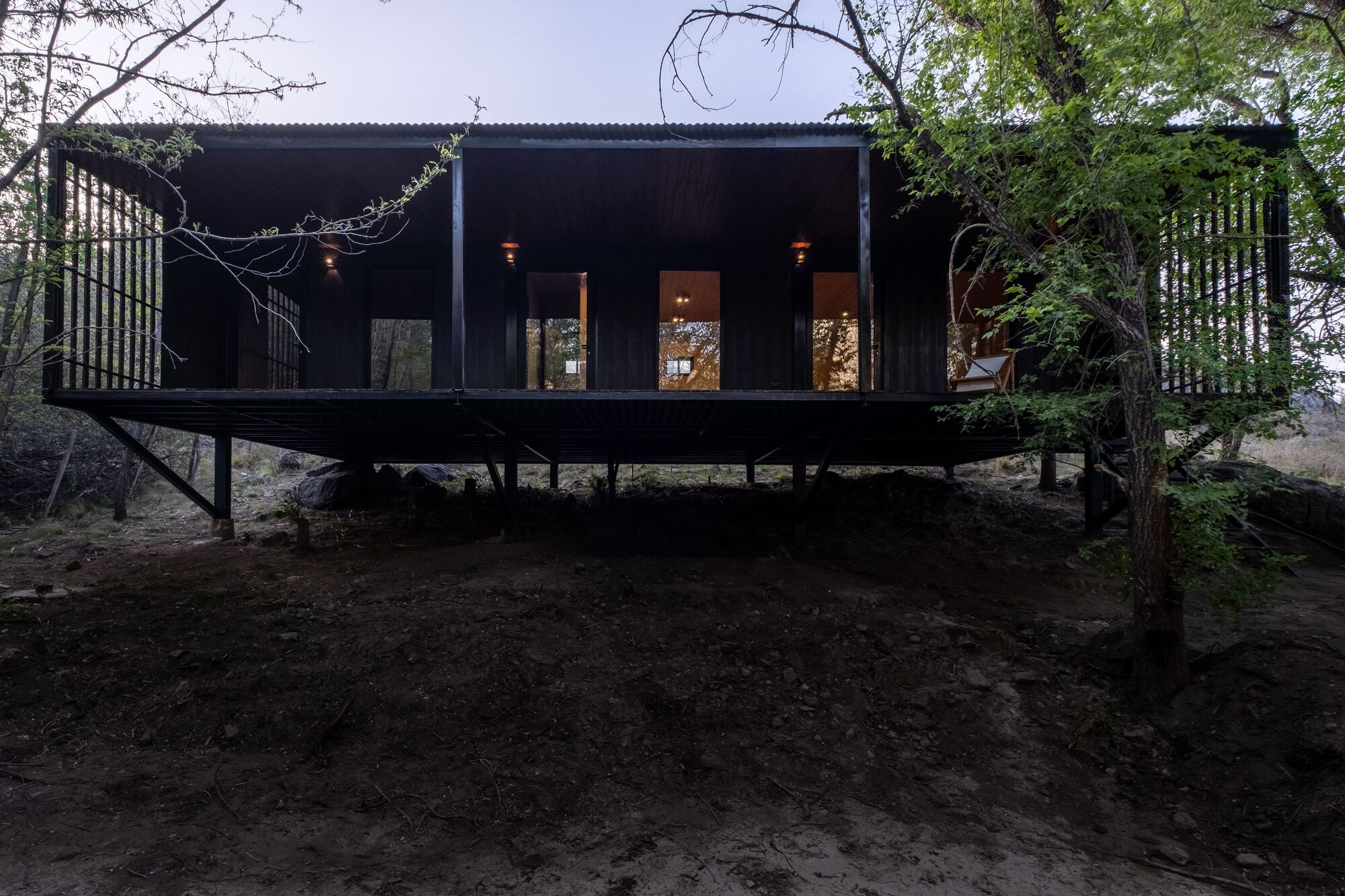 Elevated black timber pavilion on steel columns with vertical screen facades at dusk