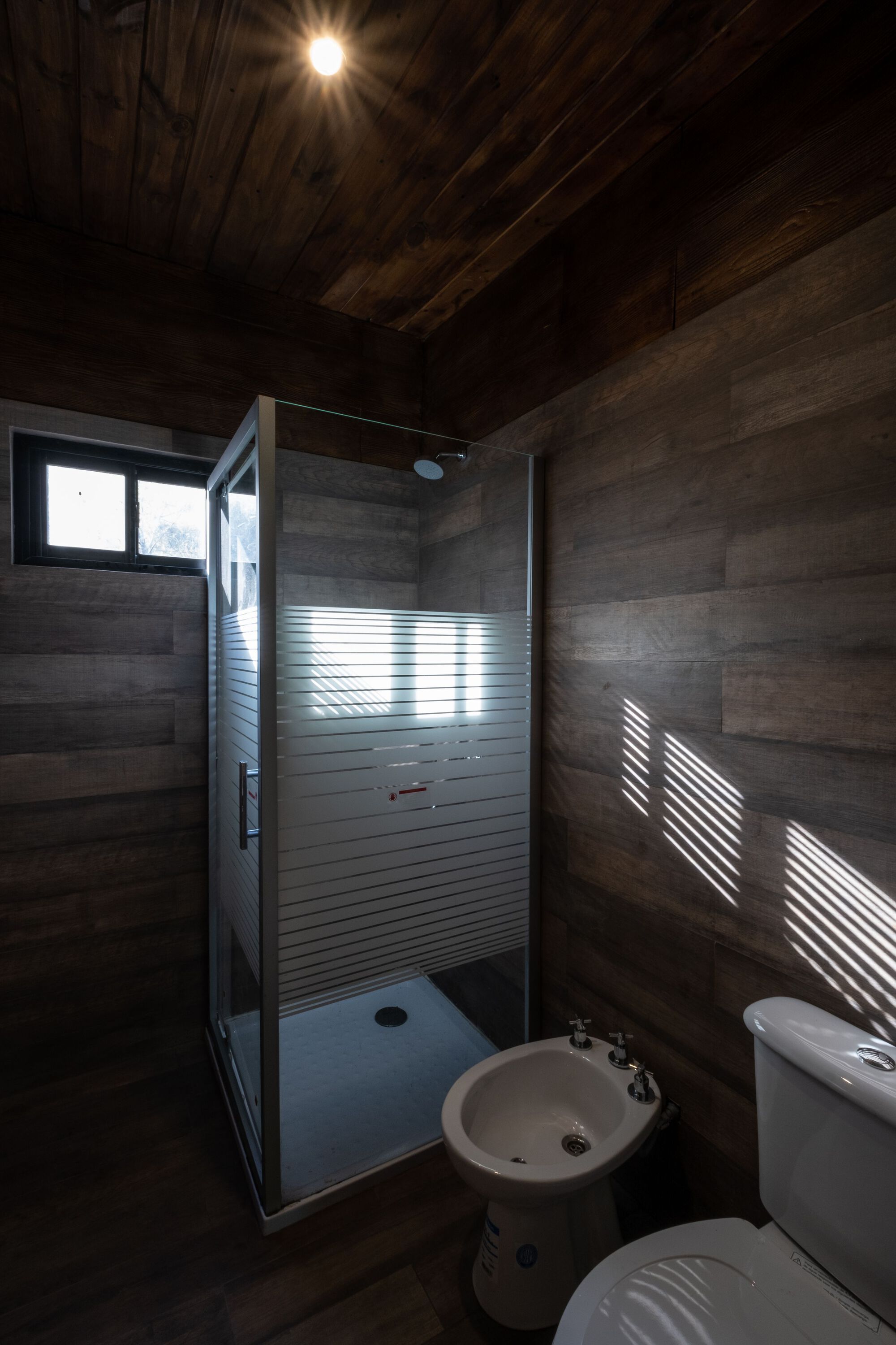 Bathroom with horizontal wood cladding and striped light through a frosted glass shower door