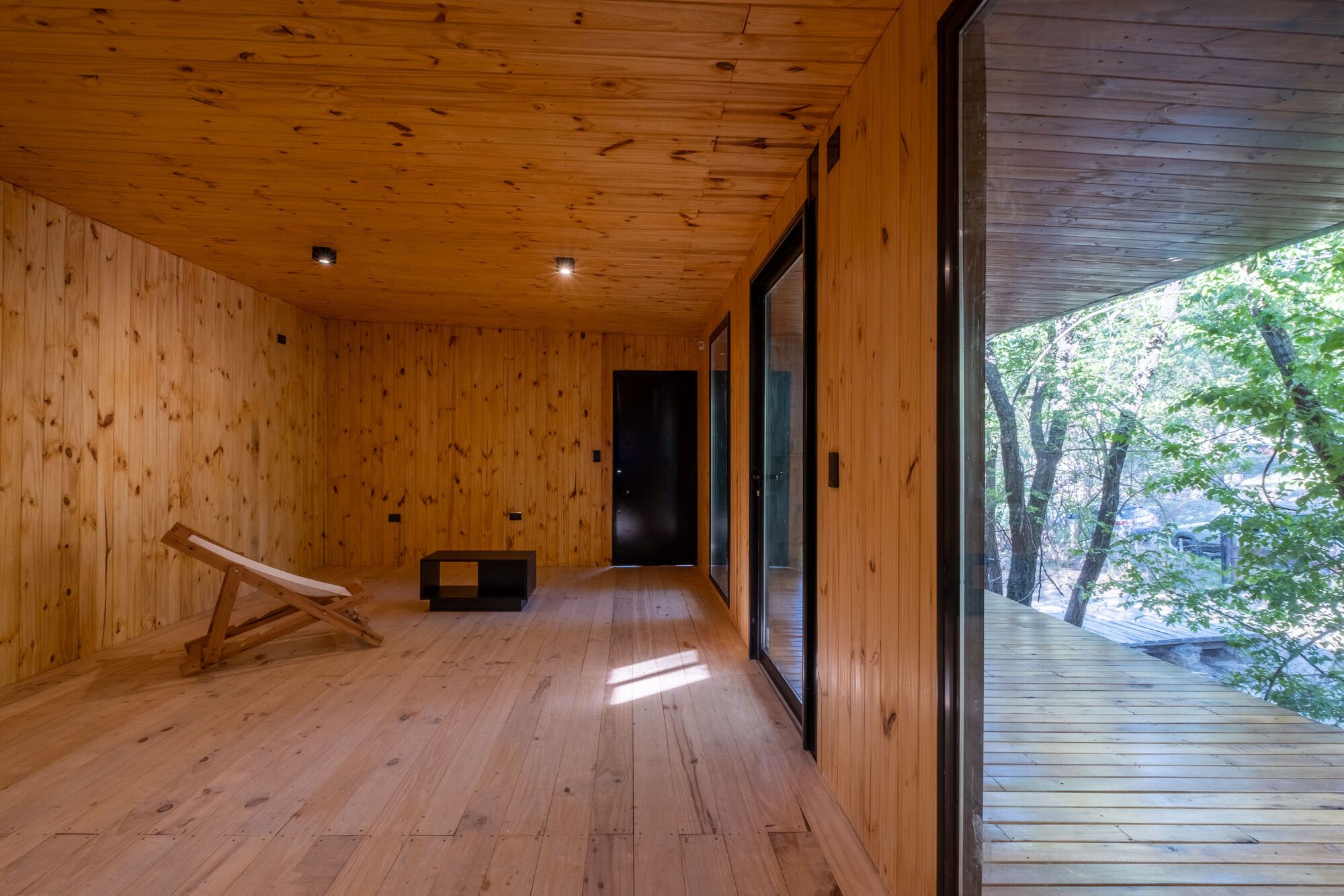 Pine plank hallway with a canvas chair and open sliding door to the forest